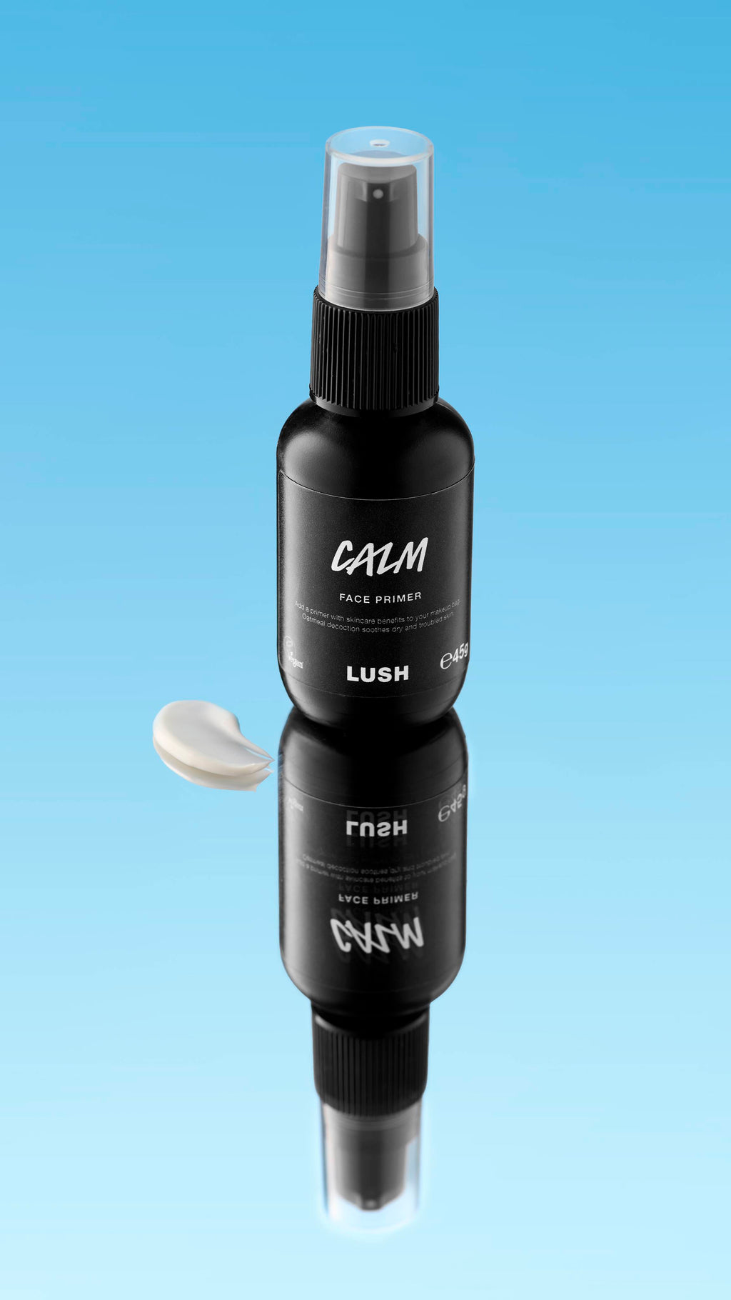 An angled product shot of a black spray bottle of LUSH Calm Face Primer, standing on a reflective surface. A creamy white swatch of the product rests next to the bottle and its reflection, all against a bright blue background.
