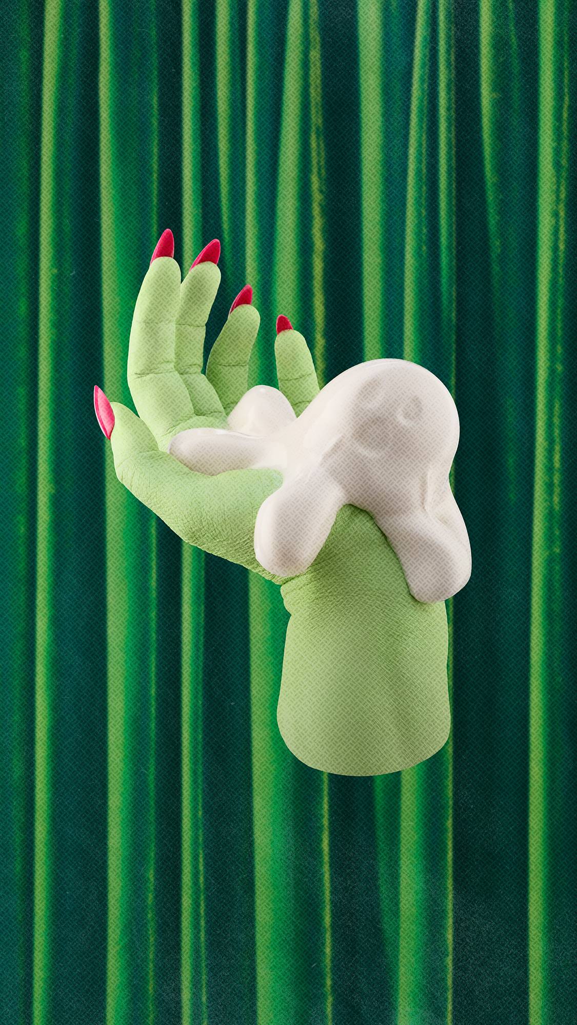 A pale green witch's hand with long, bright pink fingernails holds a smooth, white ghost-shaped shower jelly product. The scene is set against a background of pleated, deep green velvet curtains.