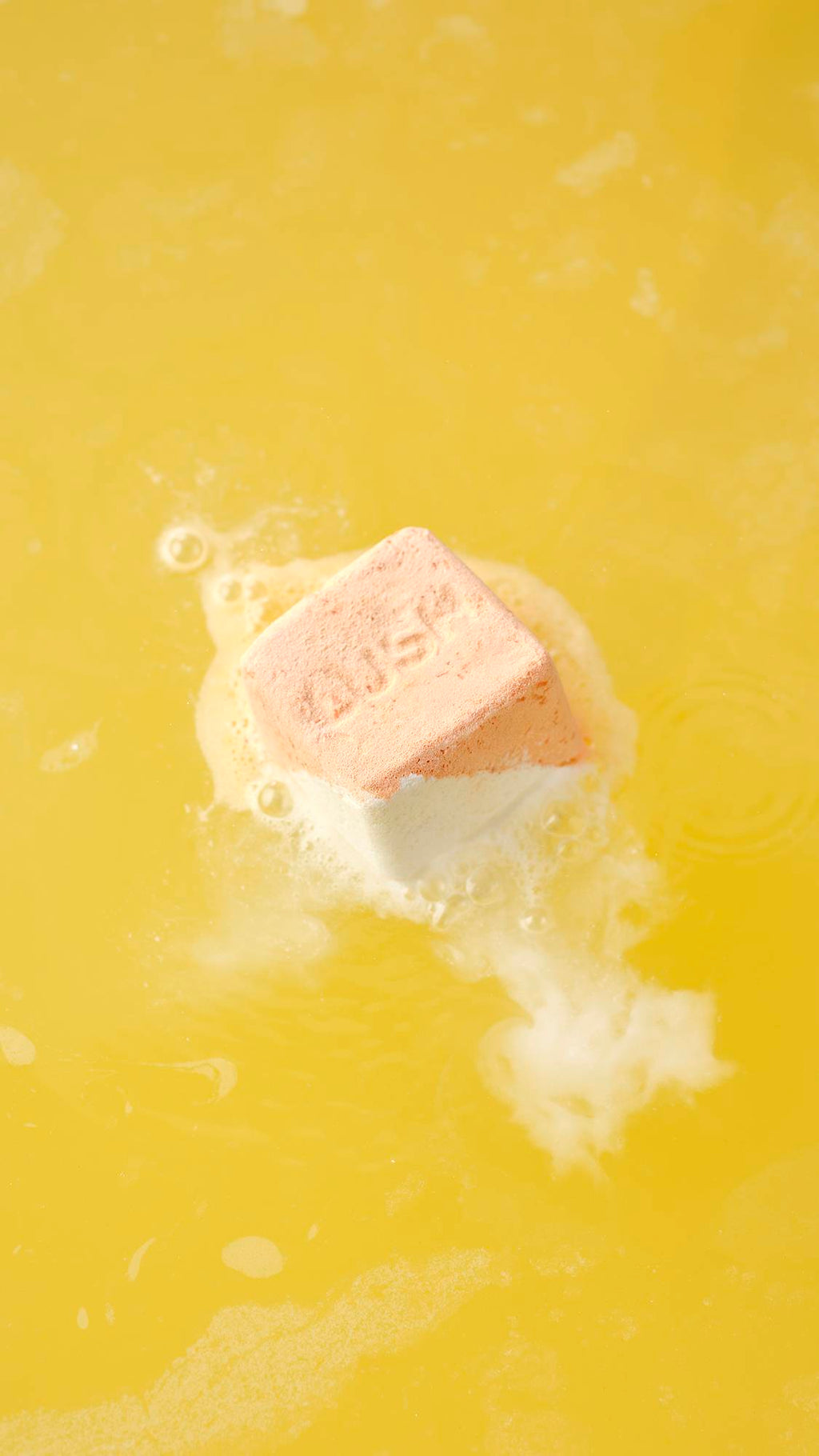 The Cold Water Soother bath bomb dissolves on the surface, releasing white, frothy foam and vibrant swirls that ripple across the water.