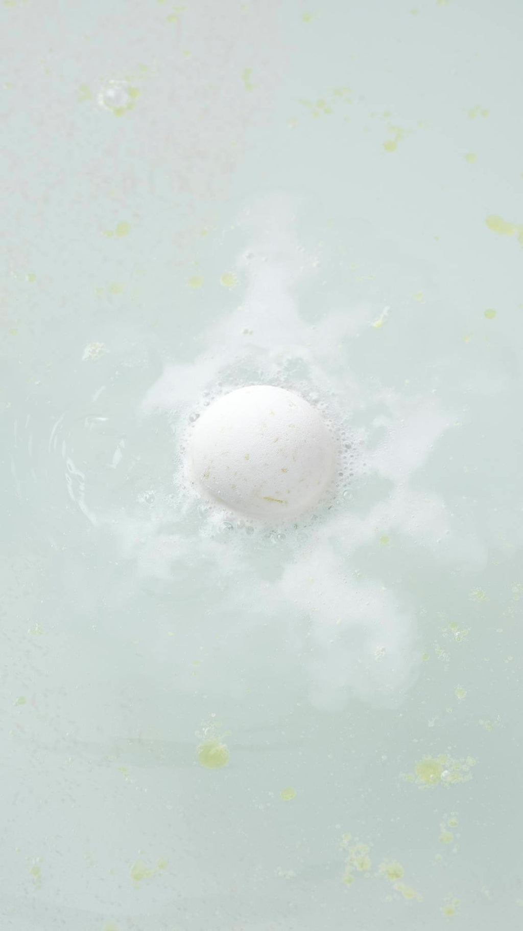 The white, spherical Butterball bath bomb sits on a plain, light gray background. The product features a matte, slightly textured surface with small, visible brown flecks of cocoa butter throughout.