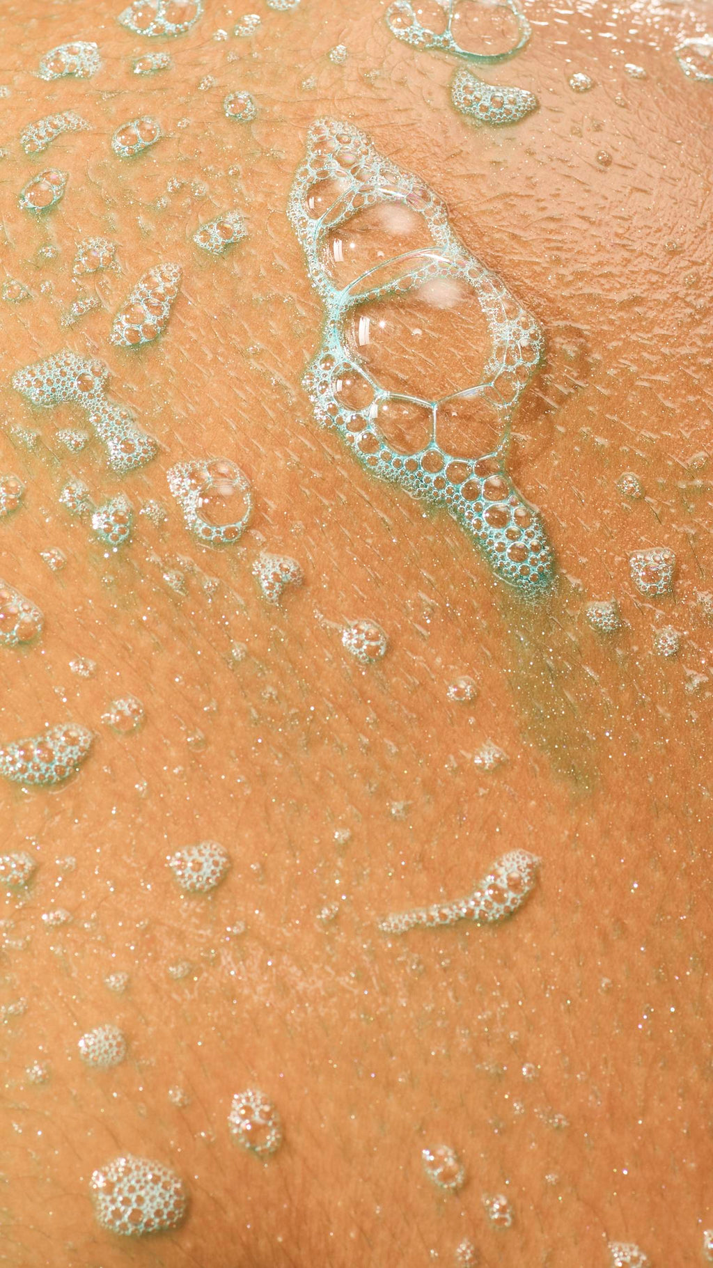 A close-up of wet, glistening skin covered in light teal soapy lather and clusters of translucent bubbles.