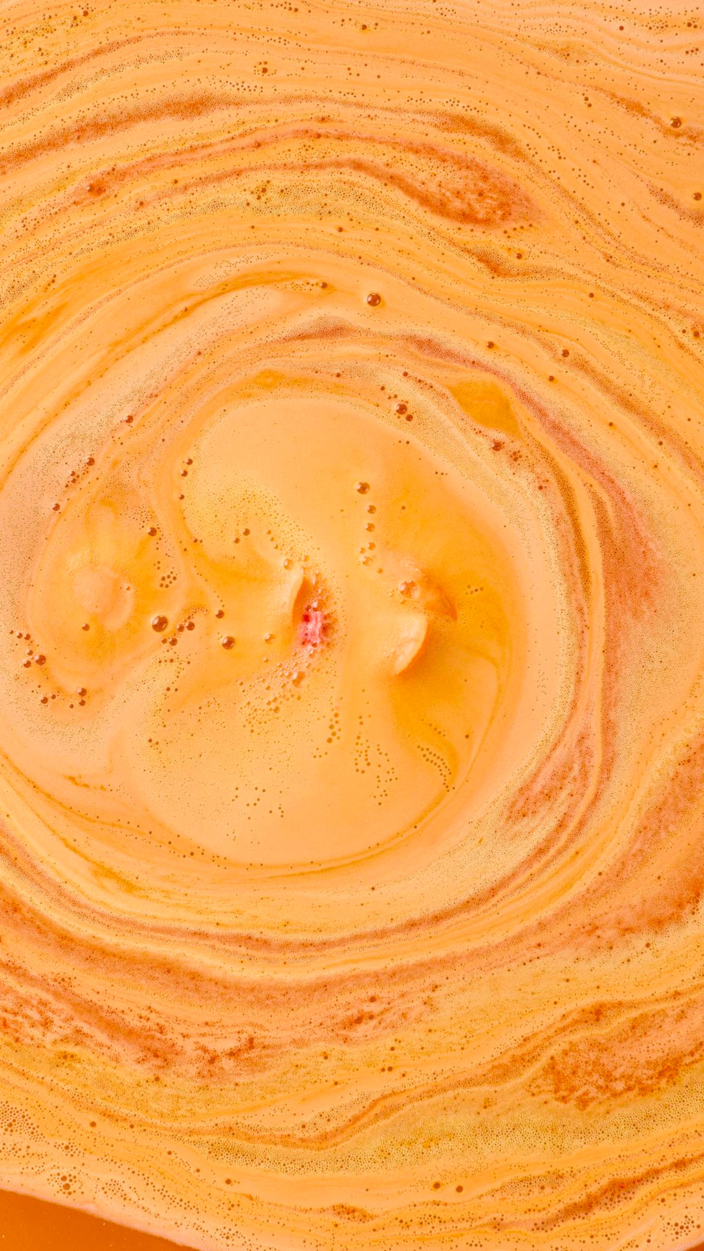 Top-down view of a dissolved Peachy Bath Bomb creating mesmerizing swirls of vibrant orange and golden foam with tiny bubble trails.
