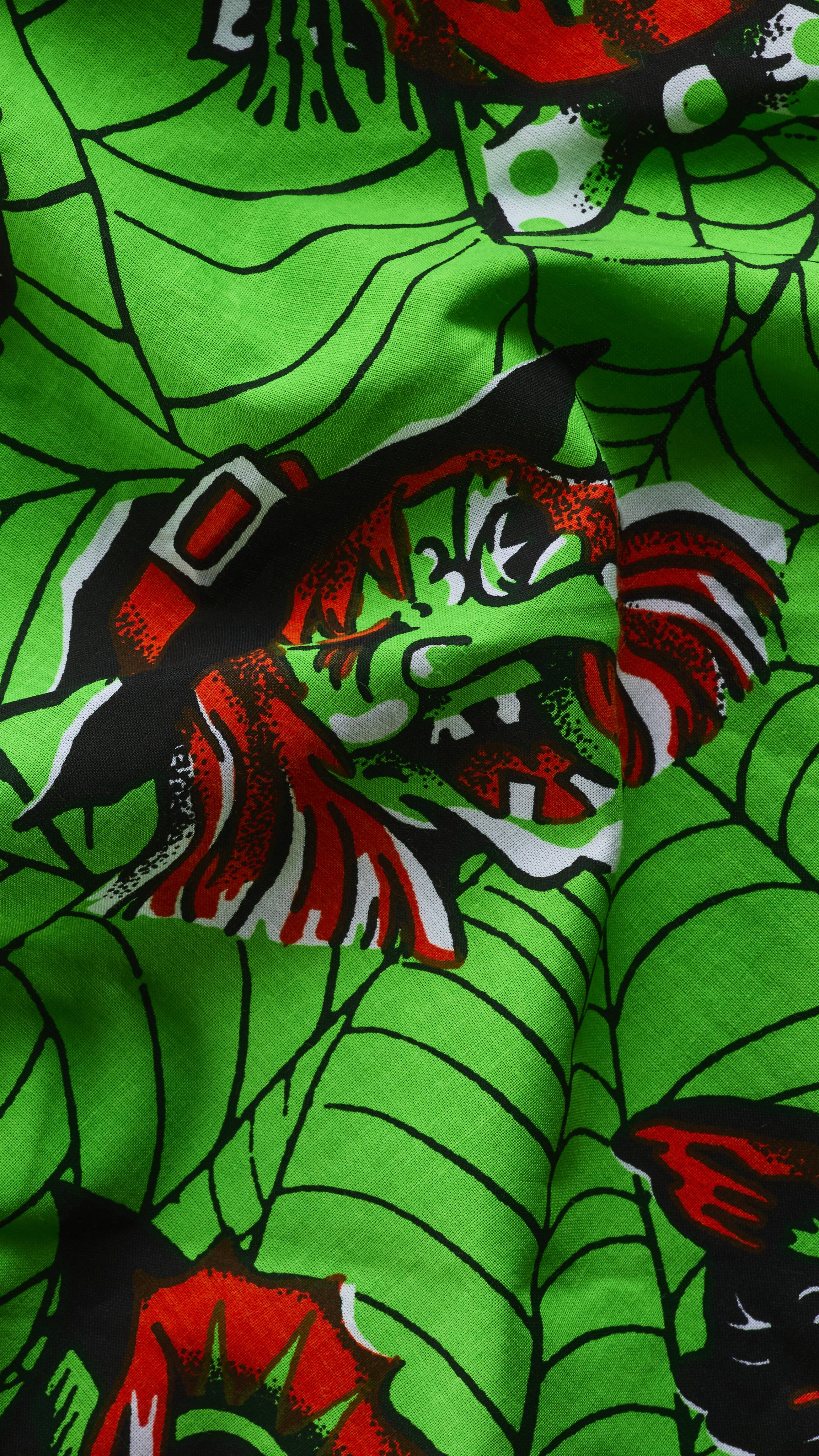 A close-up of a rumpled bright green fabric knot wrap with a black cobweb pattern. The fabric features a vintage-style illustration of a green-faced witch wearing a black and red pointy hat with a buckle.