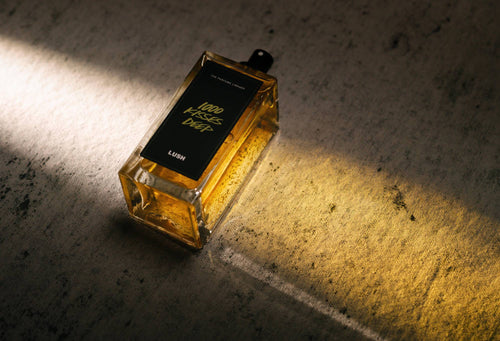 1000 Kisses Deep, a bottled, black label perfume, lies flat, with light shining through it, creating a golden cast of light.