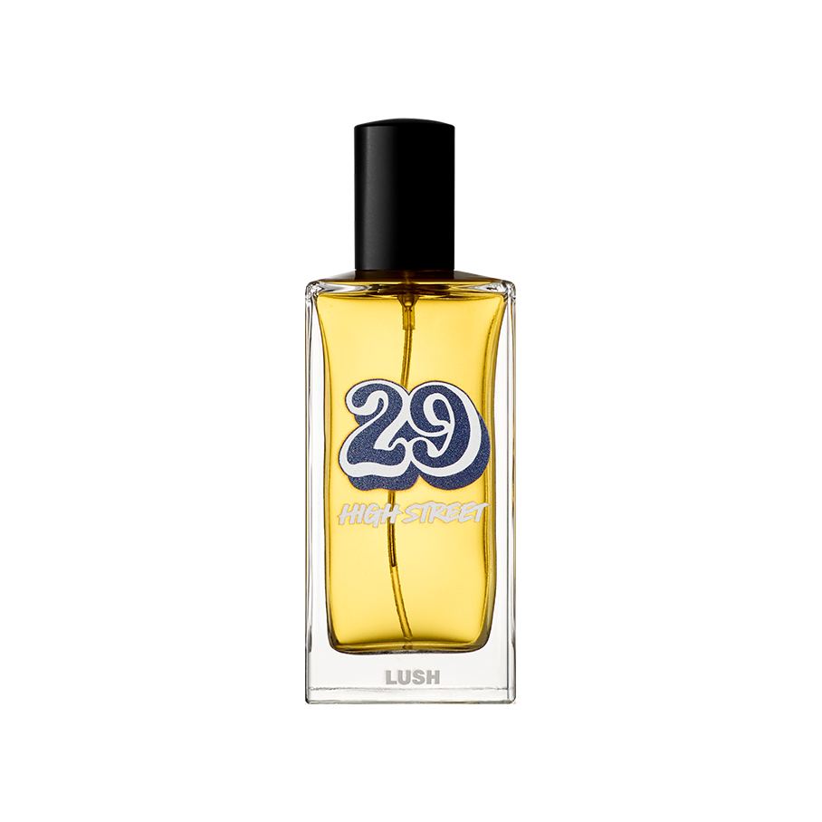 29 High Street. A rectangular glass perfume bottle containing a yellow liquid perfume, featuring a black cylindrical cap. The label shows a large, retro-style blue number '29' with 'HIGH STREET' and the 'LUSH' logo in white text.