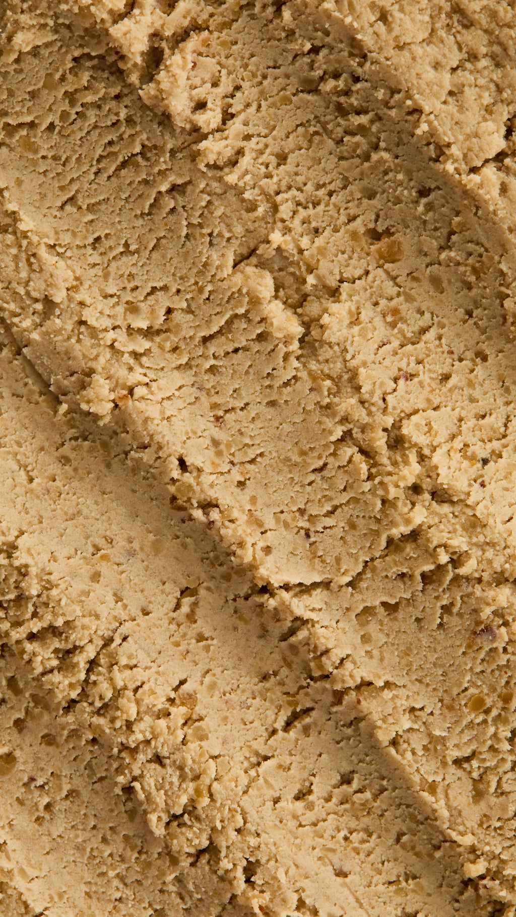 A super close-up image of the sand/ivory-coloured, textured Biomic facial cleanser, focusing on the consistency of grainy dough.