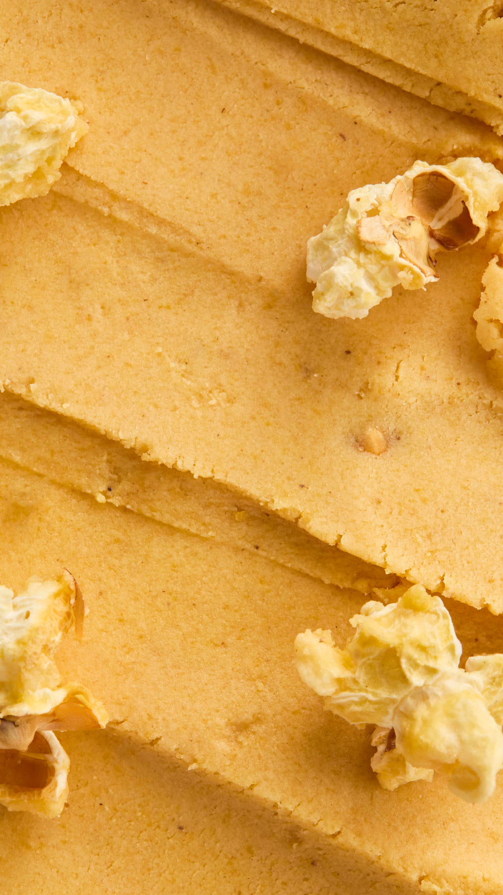 Extreme close-up vertical shot of the thick, yellow, dough-like texture of the Let the Good Times Roll Cleanser, showing visible streaks and embedded pieces of white, popped popcorn