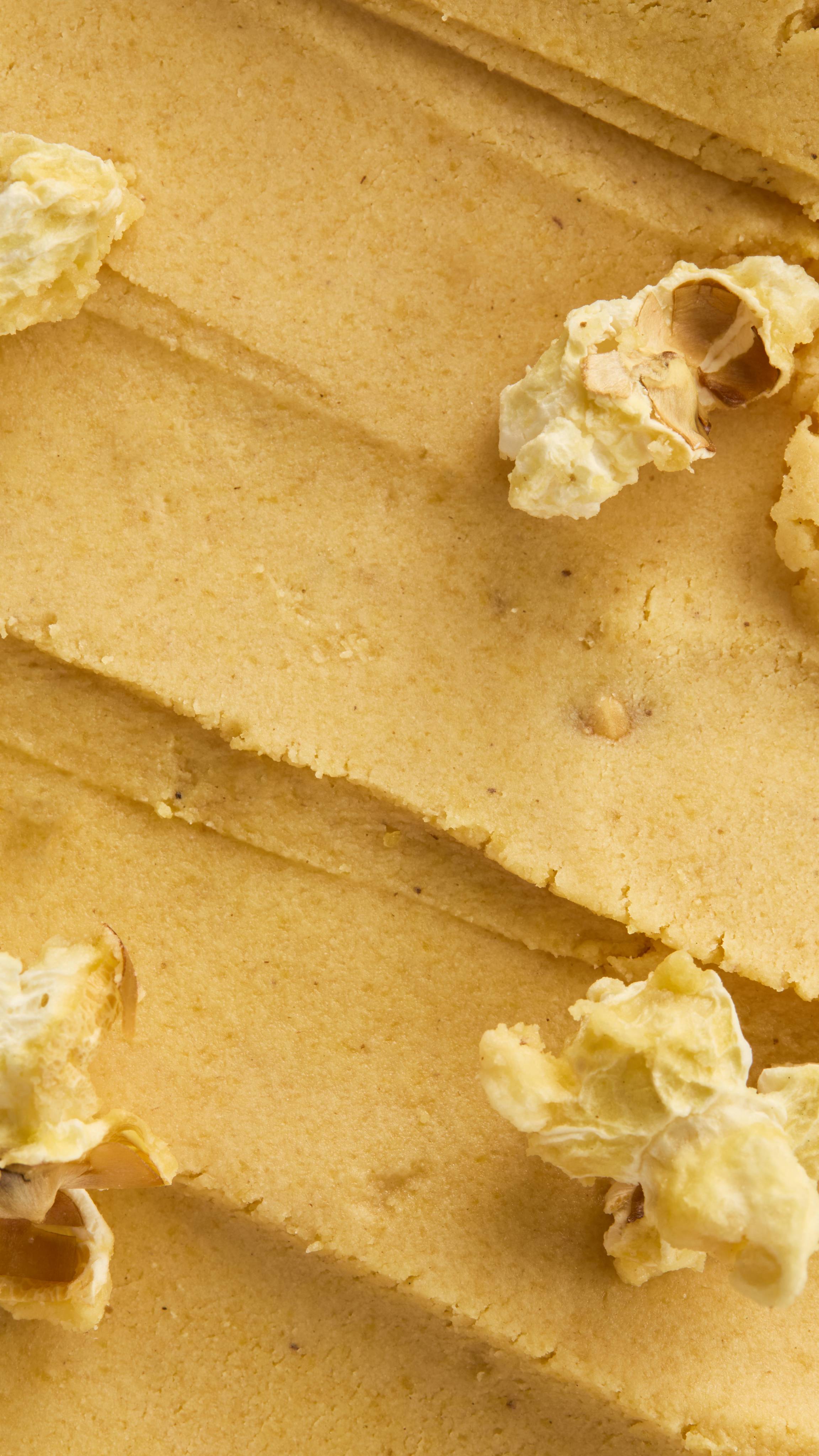 Extreme close-up vertical shot of the thick, yellow, dough-like texture of the Let the Good Times Roll Cleanser, showing visible streaks and embedded pieces of white, popped popcorn