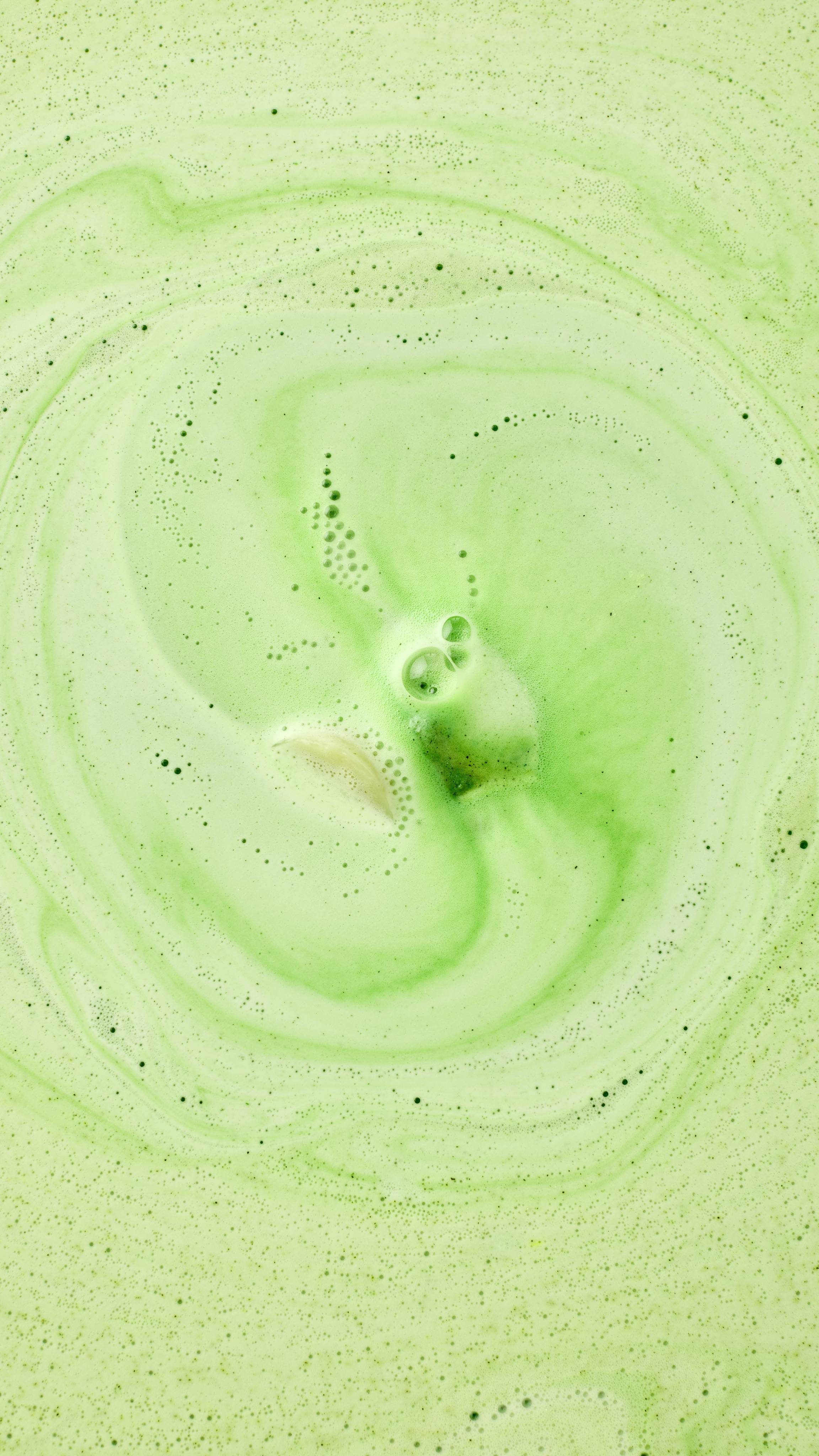 A top-down view captures the Cold Bath Bomb dissolving in the water, creating a mesmerizing swirl of frothy green and creamy white foam.