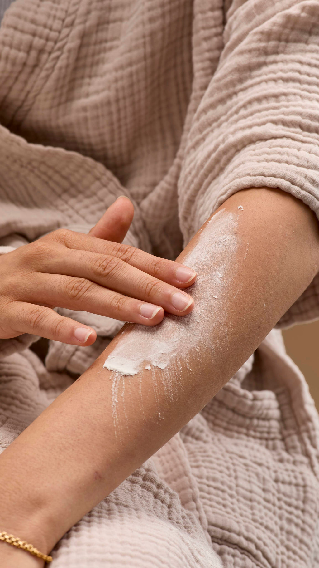 The image shows a hand rubbing a broad smear of pale cream 'Silky Underwear' dusting powder onto a bare forearm. The person wears a light-coloured robe and bracelet against a solid beige background.