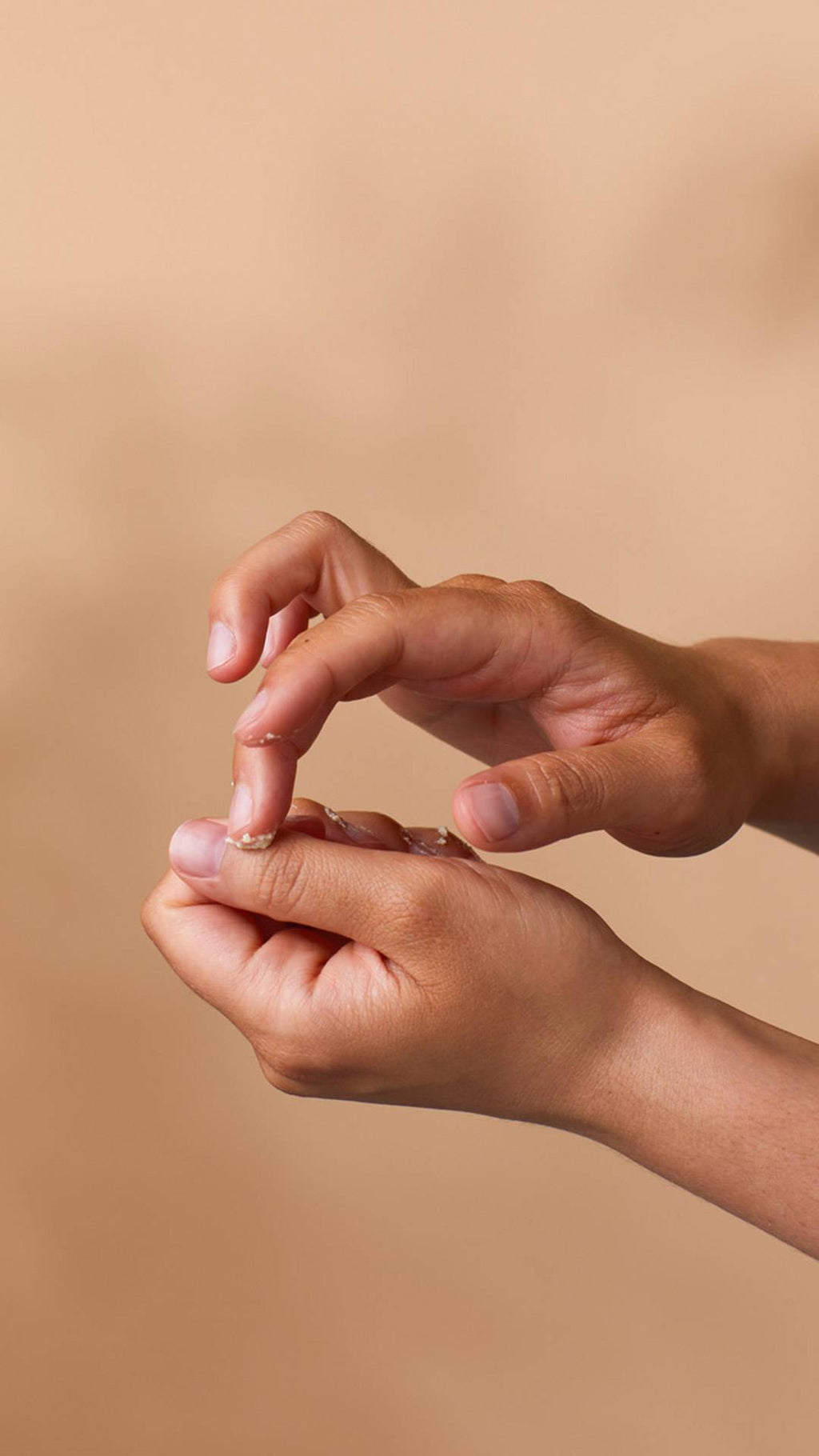 A close-up of a person's hands against a tan background, showing the application of "Lemony Flutter" cuticle butter. The person uses their fingertip to massage a small amount of the pale yellow cream into the cuticle of their thumb.