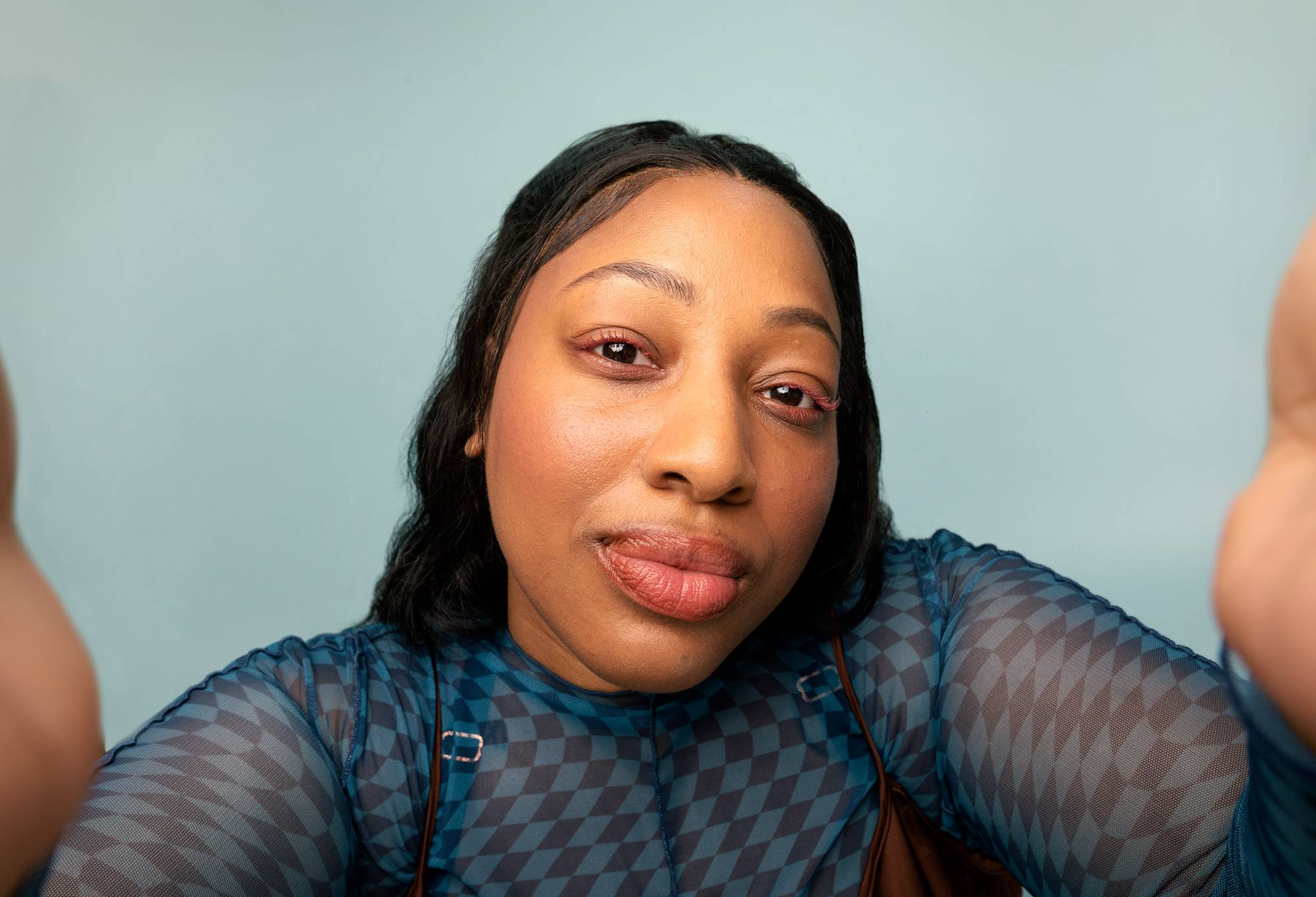 A model with gentle pink eyelashes smiles while looking face-on at the camera.