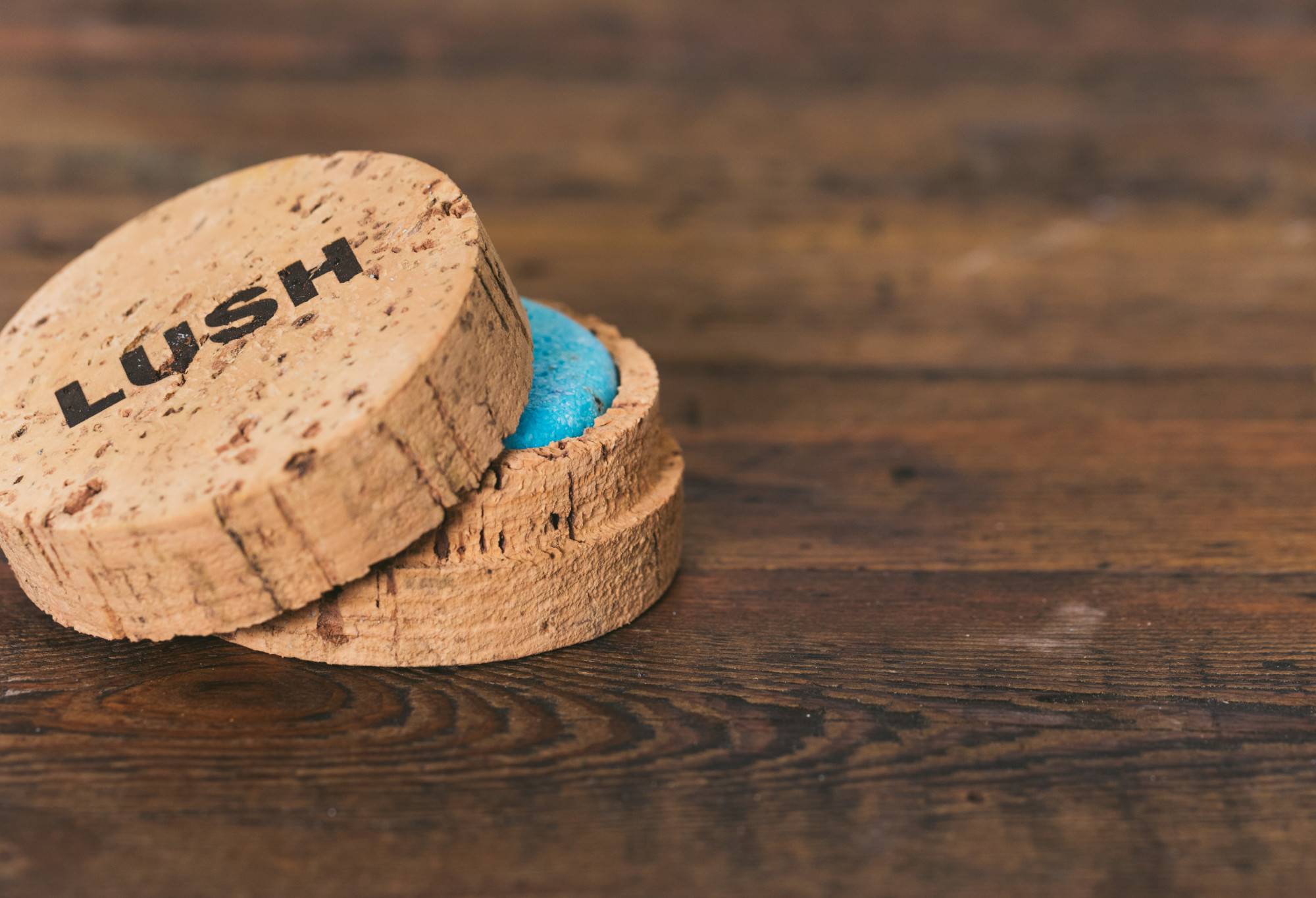 A round, natural Cork Pot product holder is being used to store a bright blue Seanik shampoo bar, just visible under the lid.
