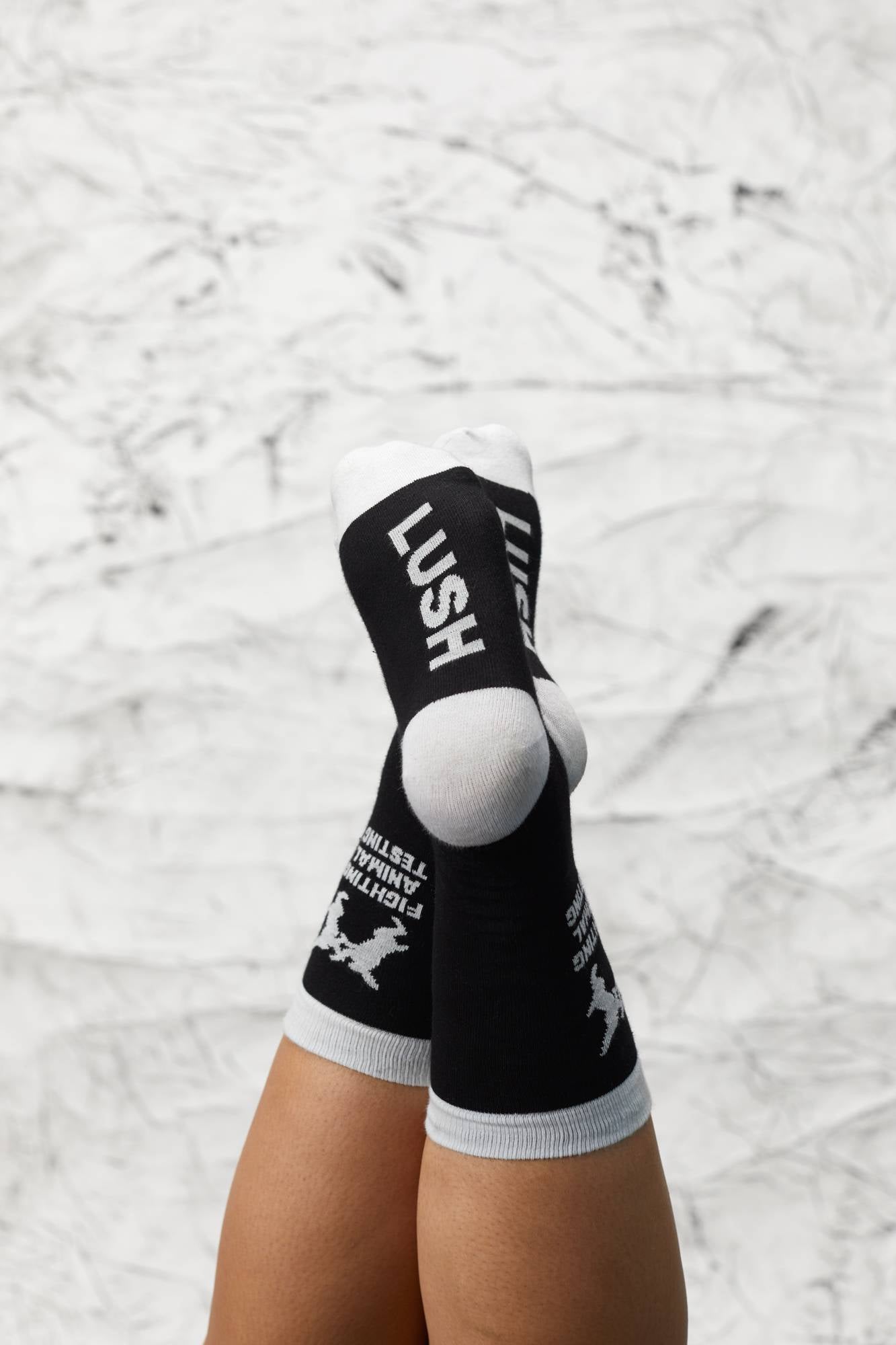 Models legs are crossed at the ankles upside down. They are wearing the socks with the "LUSH" visible on the soles.