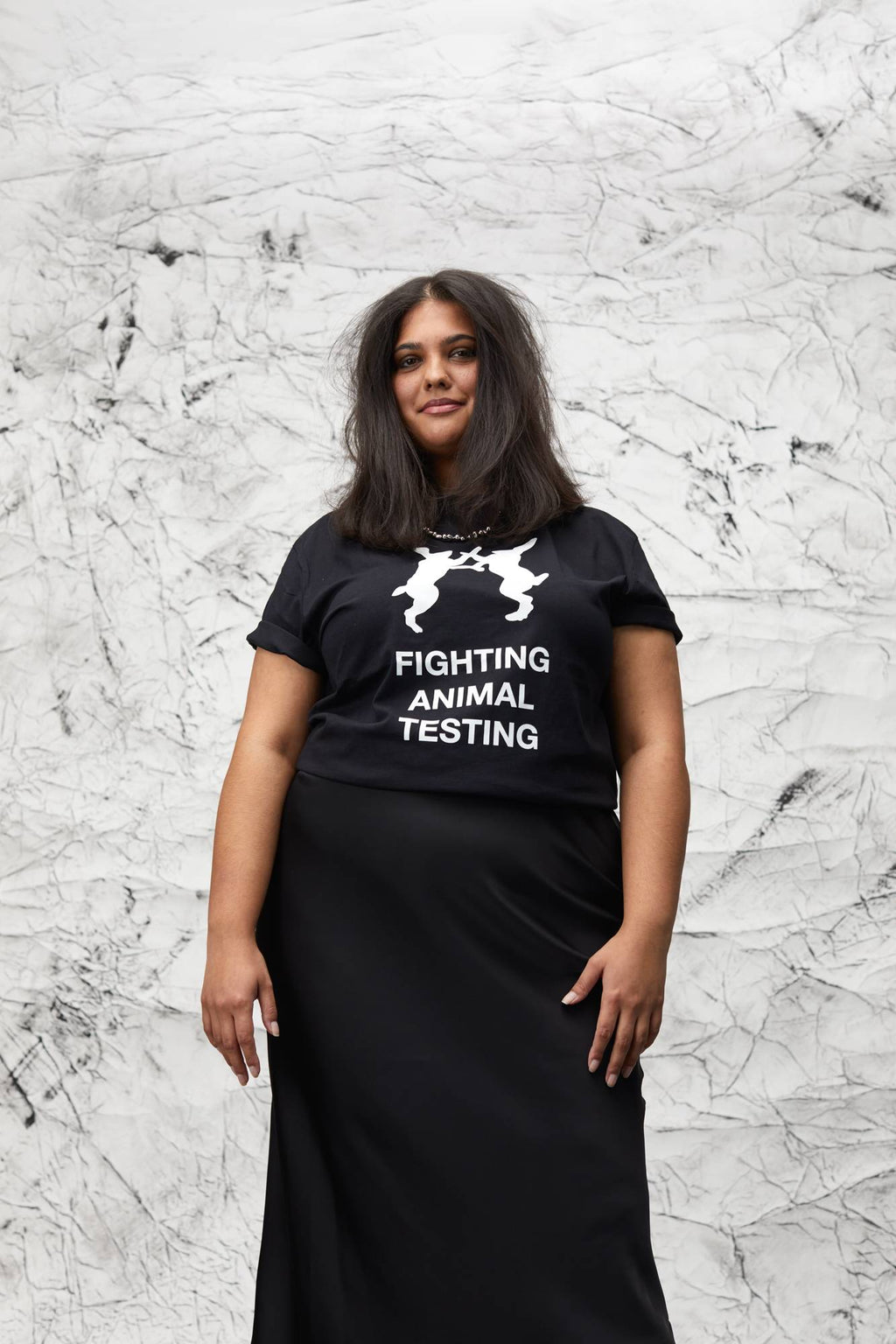 Model is stood in front of a marbled background wearing the t-shirt with a black long skirt facing frontwards.