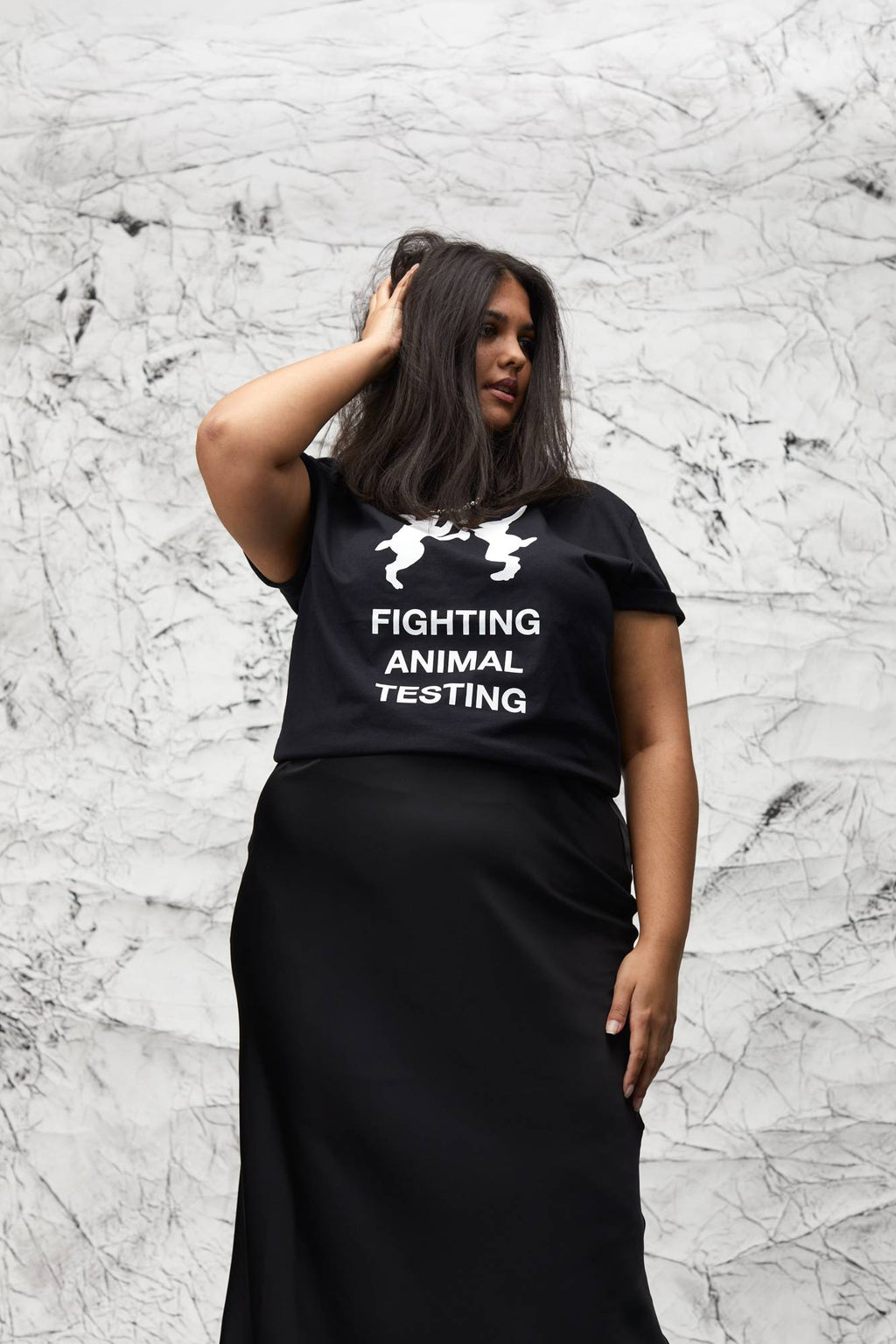 Model is stood in front of a marbled background wearing the t-shirt with a black long skirt, facing away.