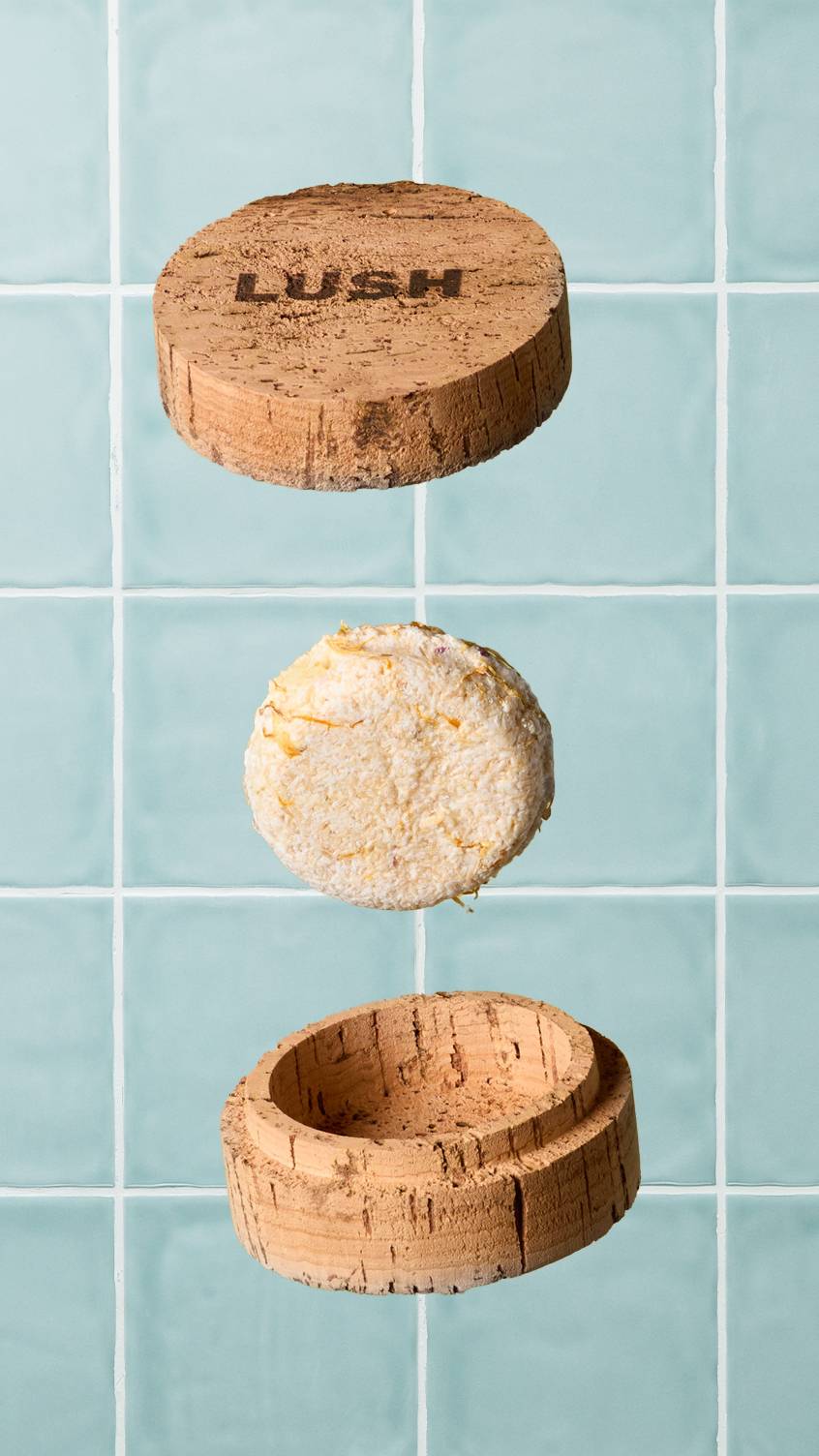 A circular, textured cream Lush shampoo bar floats vertically between an open, natural cork storage pot and its lid branded with the "LUSH" logo. The items are suspended against a backdrop of pale blue square wall tiles.