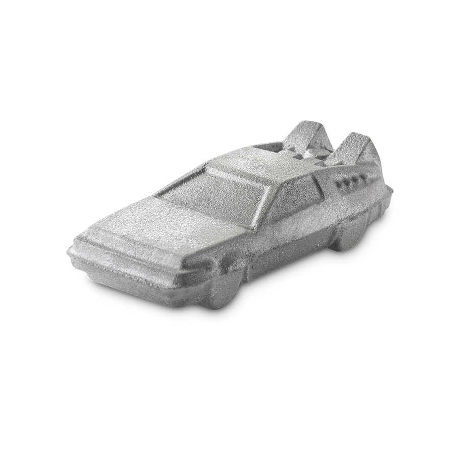 OUTATIME. A shimmering, silver bath bomb shaped like a futuristic, angular car reminiscent of a DeLorean from the nostalgic nineties films, "Back To The Future". The product has a metallic glint, and the car features detailed windows and rear fins.