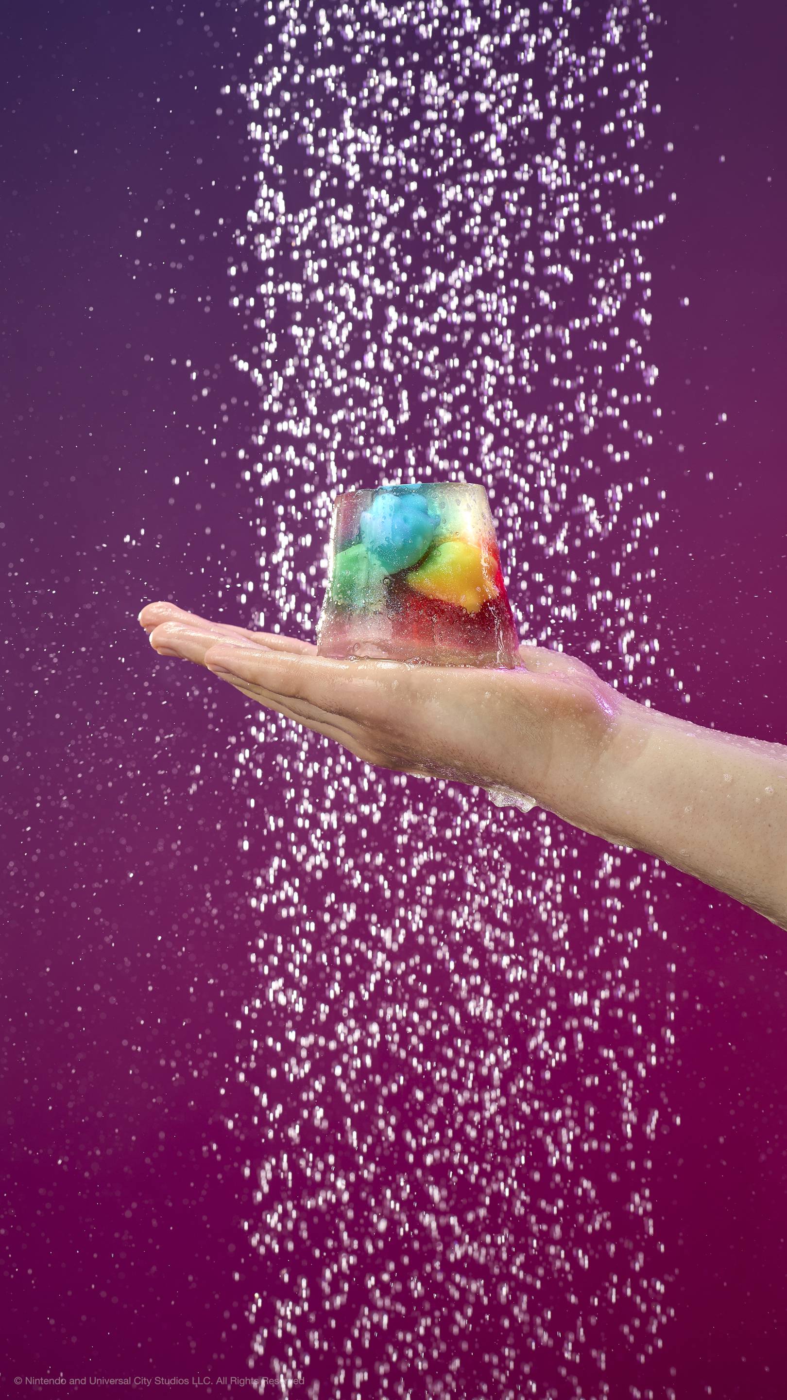A hand holds a translucent shower jelly containing colorful star-shaped Lumas under a shower spray. Against a purple-pink gradient background with shimmering plastic-free glitter.