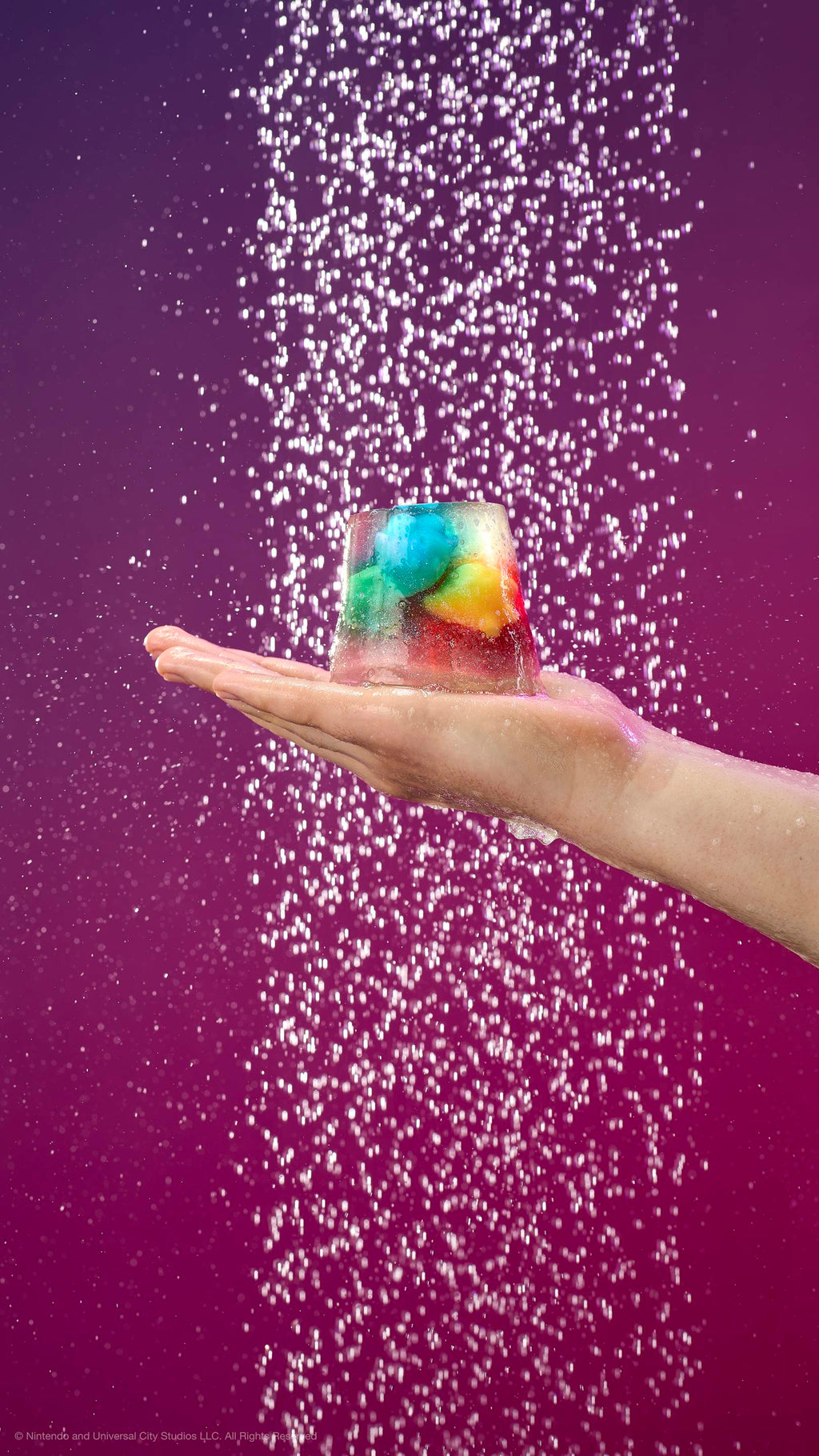 A hand holds a translucent shower jelly containing colorful star-shaped Lumas under a shower spray. Against a purple-pink gradient background with shimmering plastic-free glitter.