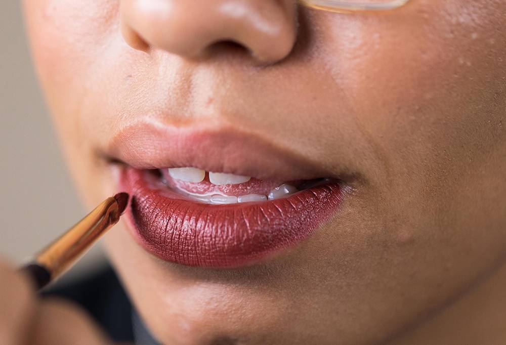 Pucker Brush, a travel lip brush, is being used to perfect the application of a shimmery, raspberry red lipstick.