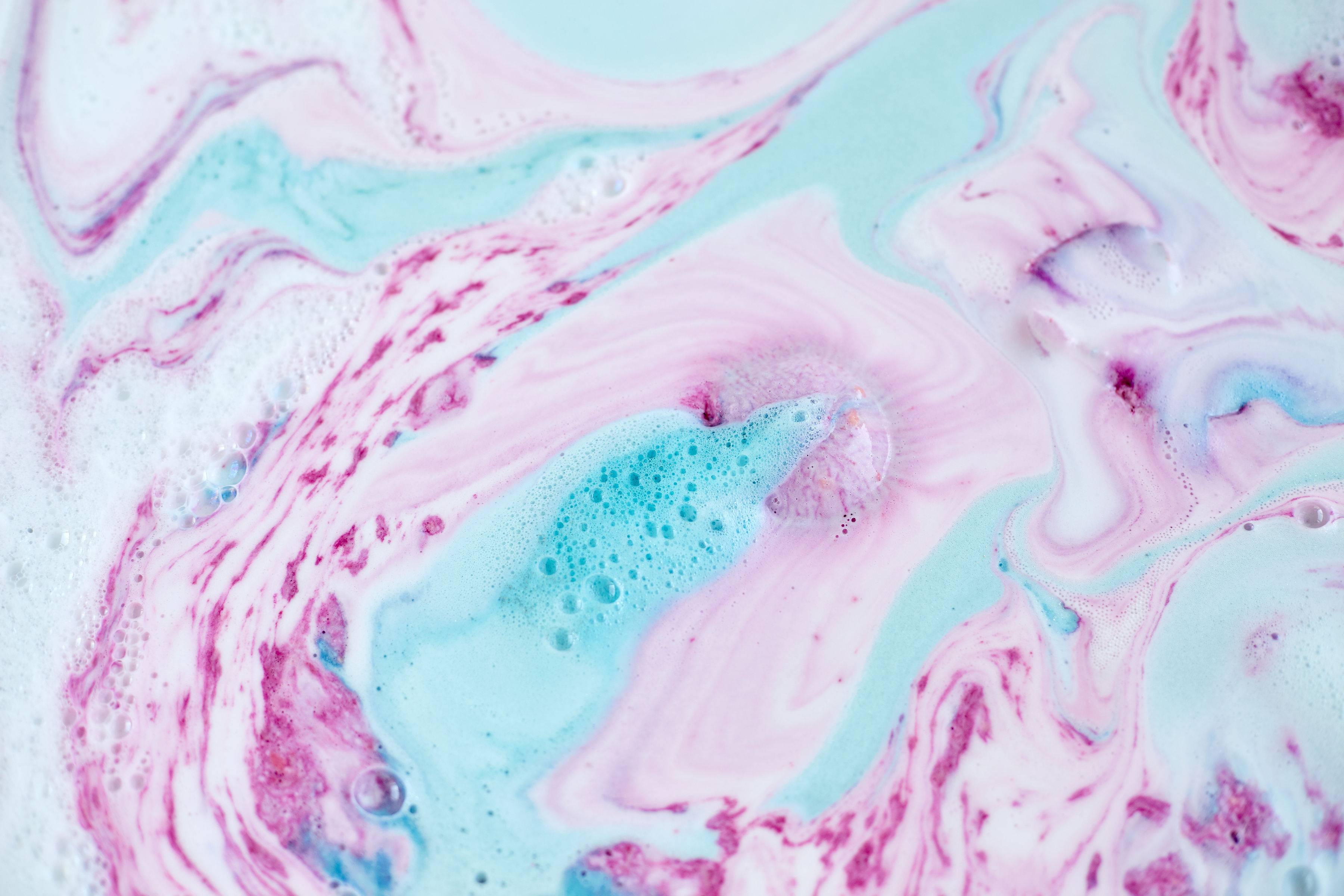 The image shows an aerial view of the bath water after using the Twilight bath bomb. There is a delicate, marbled pattern across the surface of the water made of pastel blue, pink and purple swirls of creamy, foam.