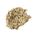A close-up, top-down studio shot of a light tan, crumbly, dough-like facial cleanser (Lush's Angels on Bare Skin) spread in a dollop on a neutral background. The textured paste is visibly studded with small, dried purple and brown lavender buds