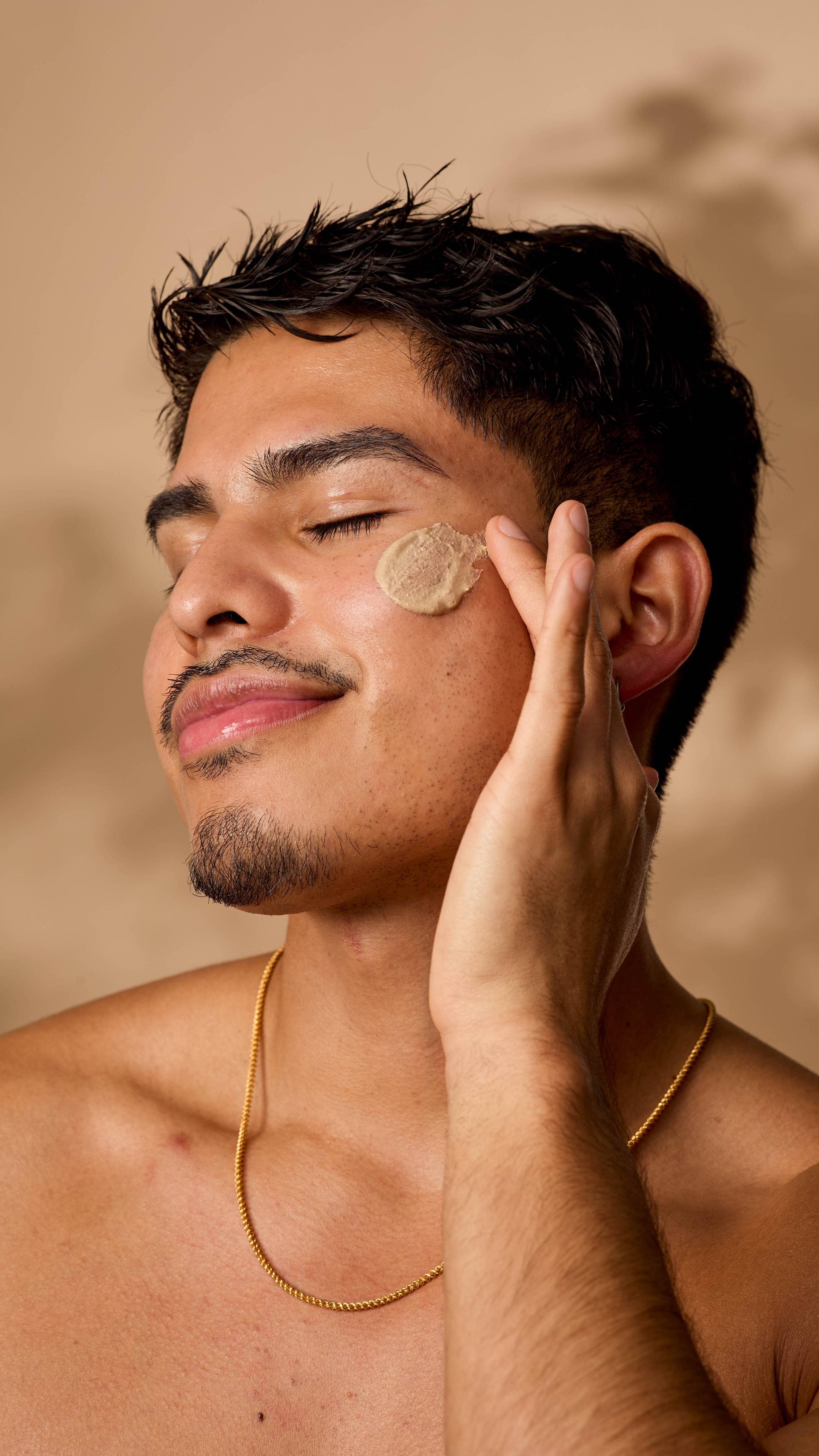 A close-up of the model's face as they gently apply the Ayesha face mask onto their cheek.