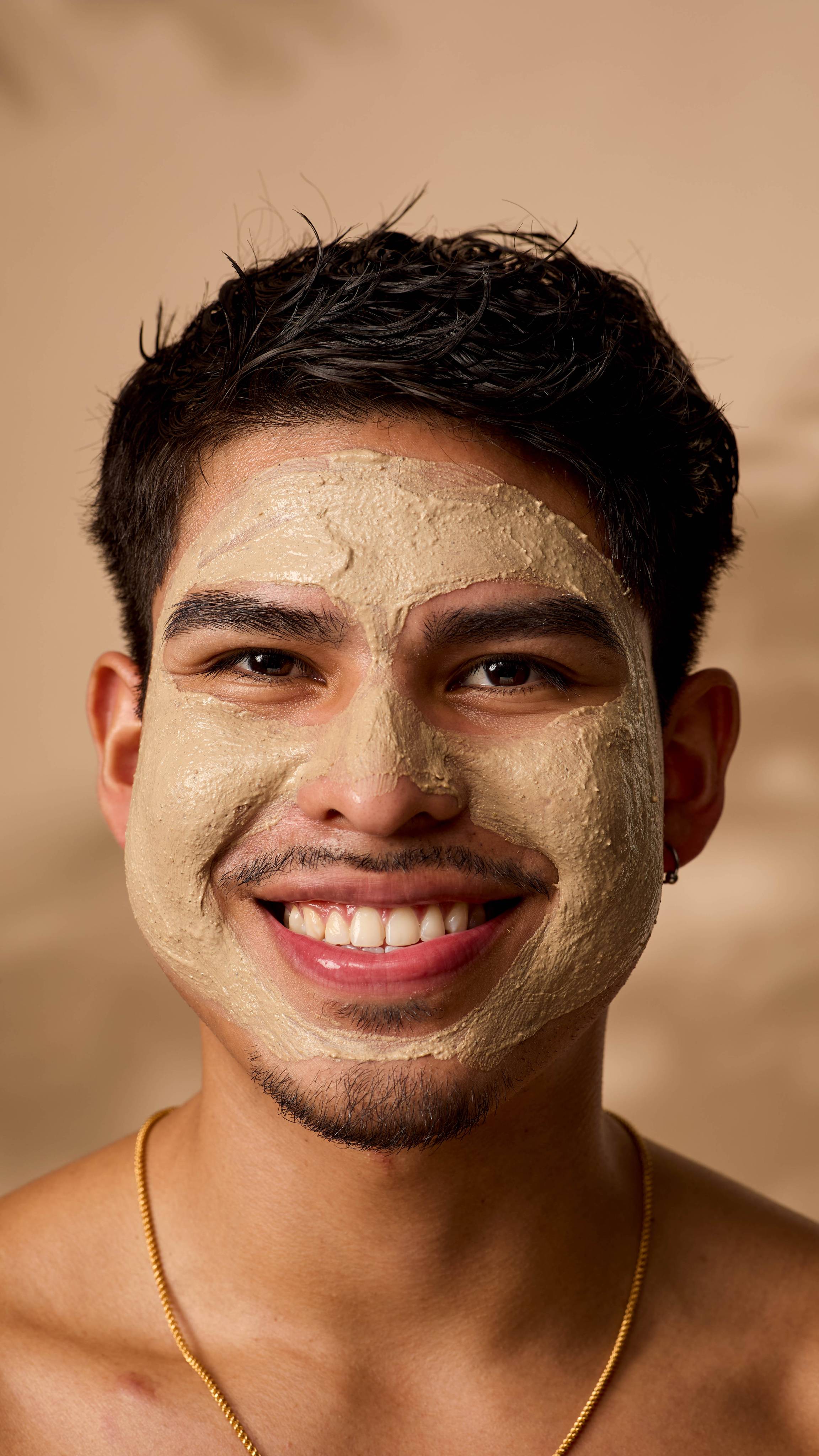 A close-up of the model smiling widely as they face the camera with the Ayesha face mask applied all over.