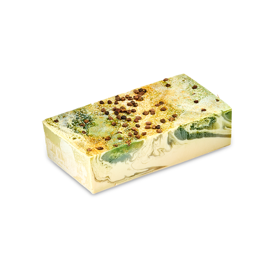 A rectangular bar of Baklava handmade soap with a cream base and marbled swirls of green and gold. The top is sprinkled with dark brown spice seeds, set against a solid black background.