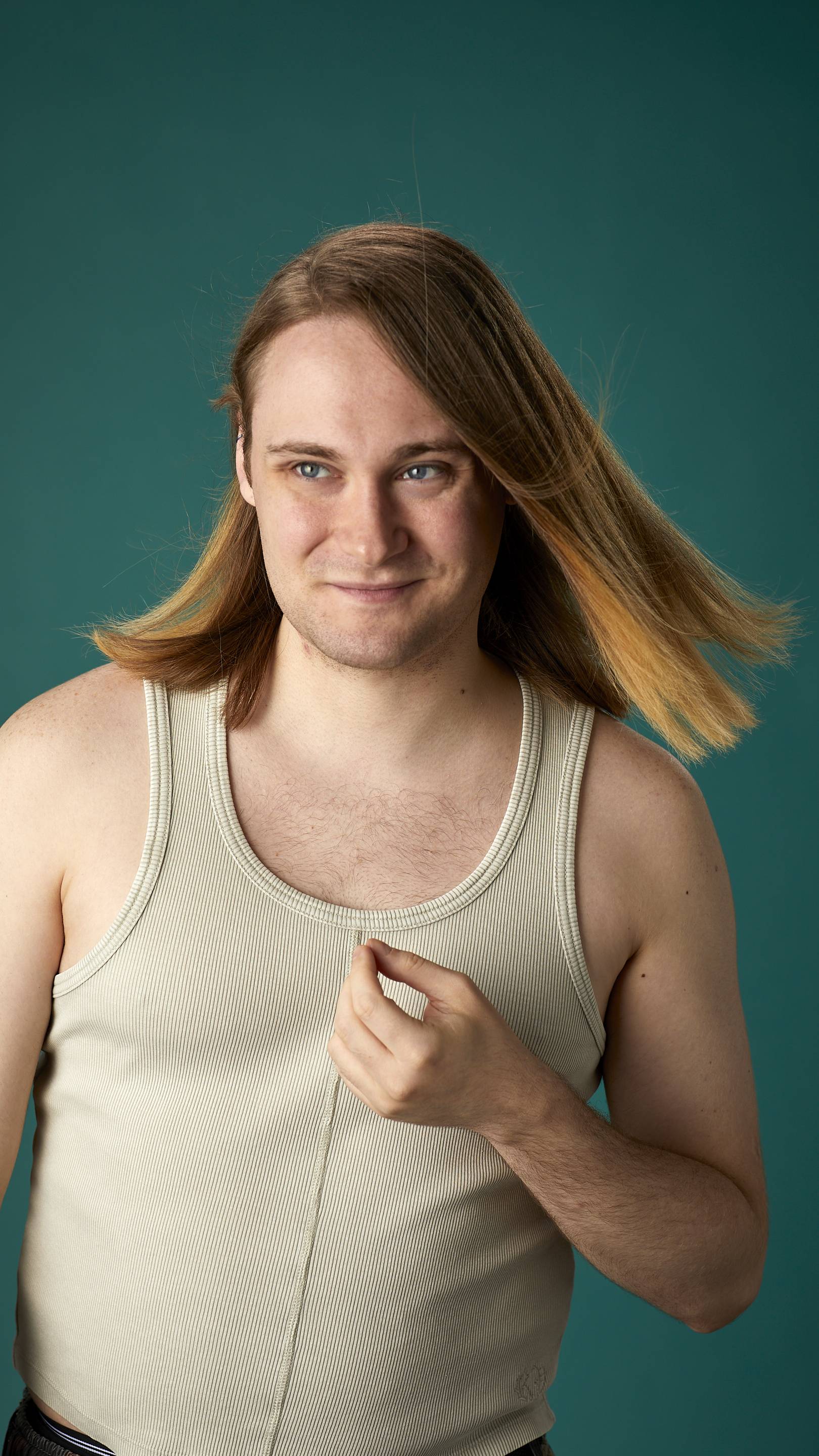 The model is on a teal background with a cream-coloured tank top. They have light brown, shoulder-length, freshly-dried hair which looks clean and healthy and is being fanned with air.