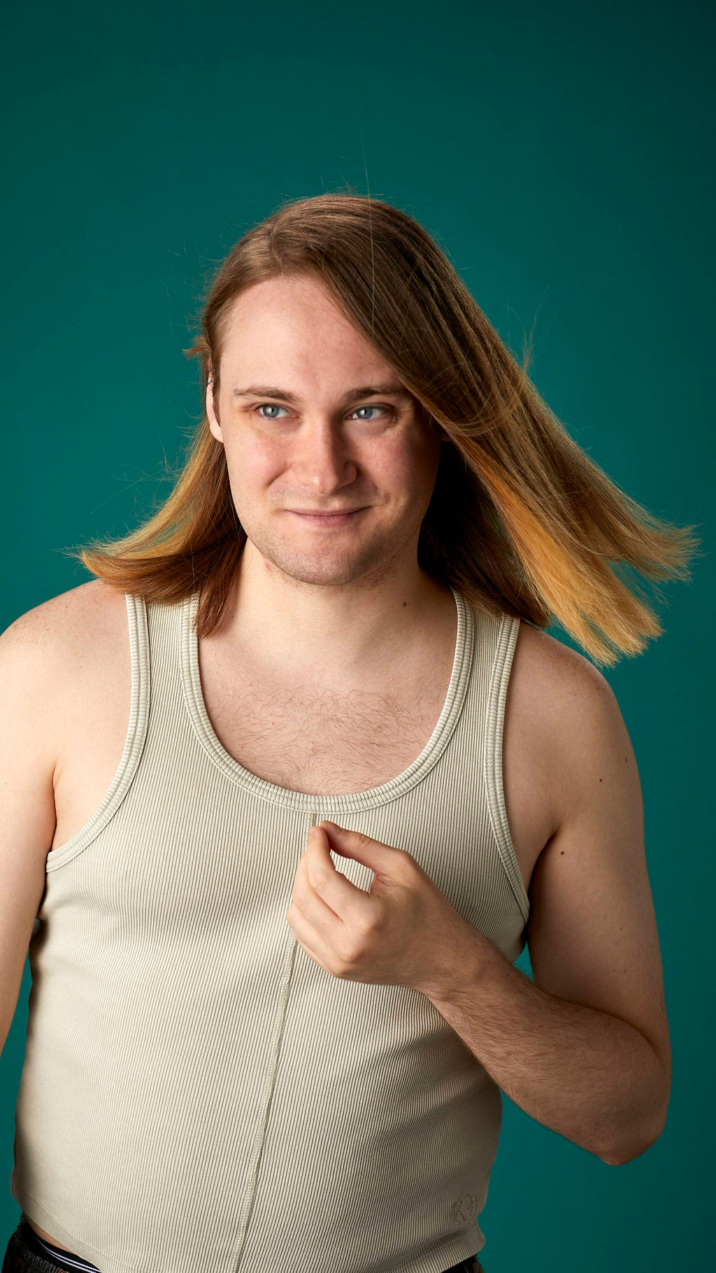 The model is on a teal background with a cream-coloured tank top. They have light brown, shoulder-length, freshly-dried hair which looks clean and healthy and is being fanned with air.