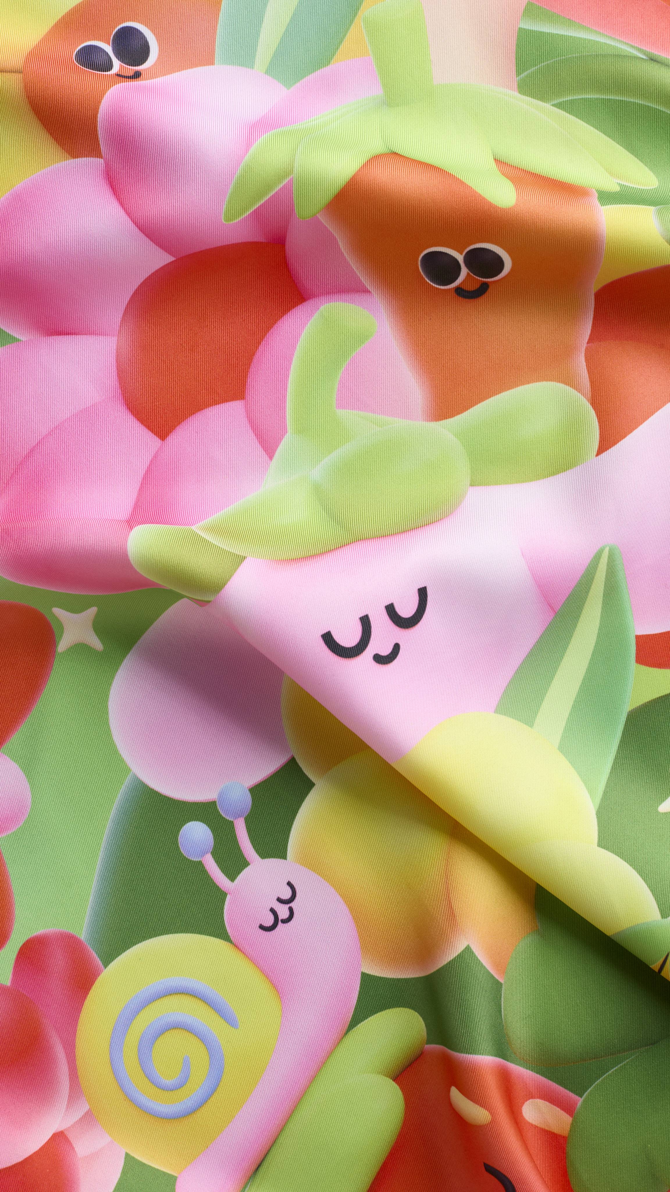 A super close-up shot of the "Blooming Lovely" fabric Knot Wrap featuring colourful, 3D-style garden illustrations. A pink snail and a smiling pink flower are visible amongst other cheerful, soft-focus garden characters.