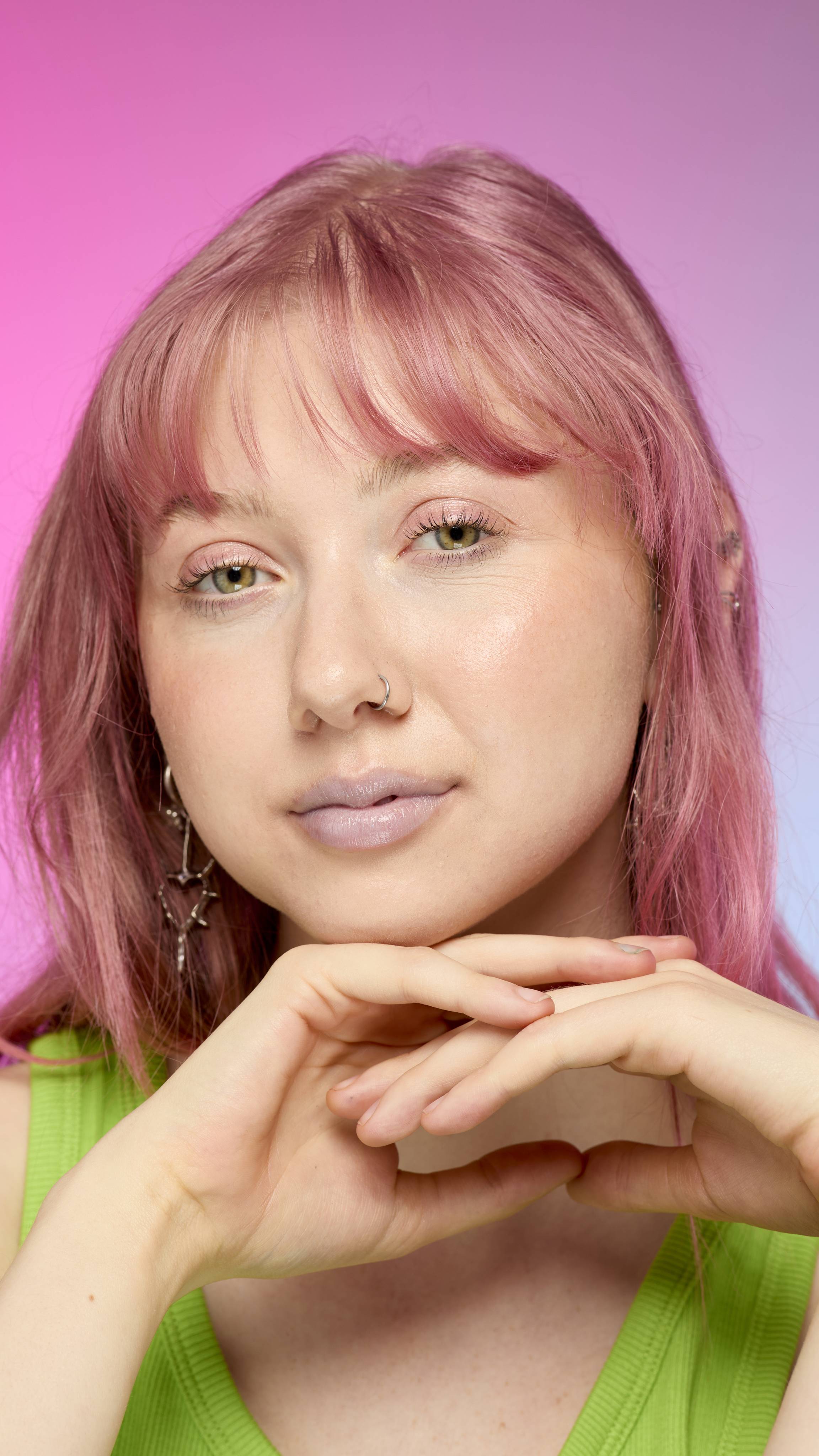 The image shows a fair-skinned model on a pink and blue gradient background. They have pink hair and subtle, blue shimmering lips from using the Blue Pearl lip cream.