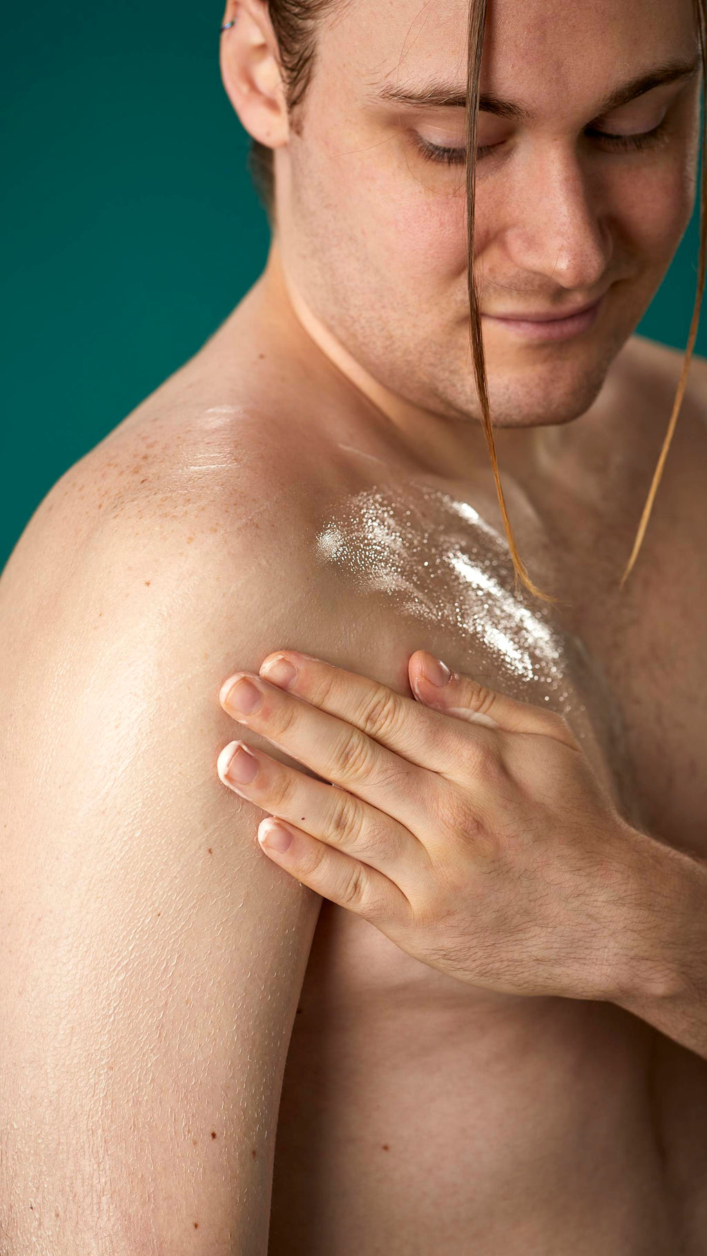 The image shows a topless model on a teal background. They are gently soothing the Braziliant body butter in circular motions over their chest and upper arm.