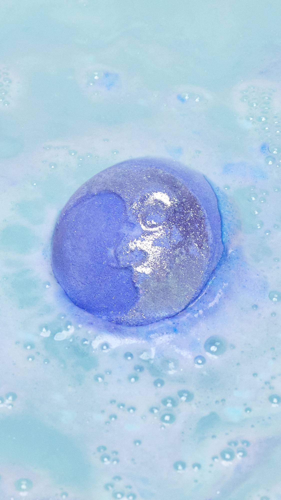 The Brother Moon bath bomb has just been placed into the bath water as it starts to give off subtle purple foam laced with silver sparkles.