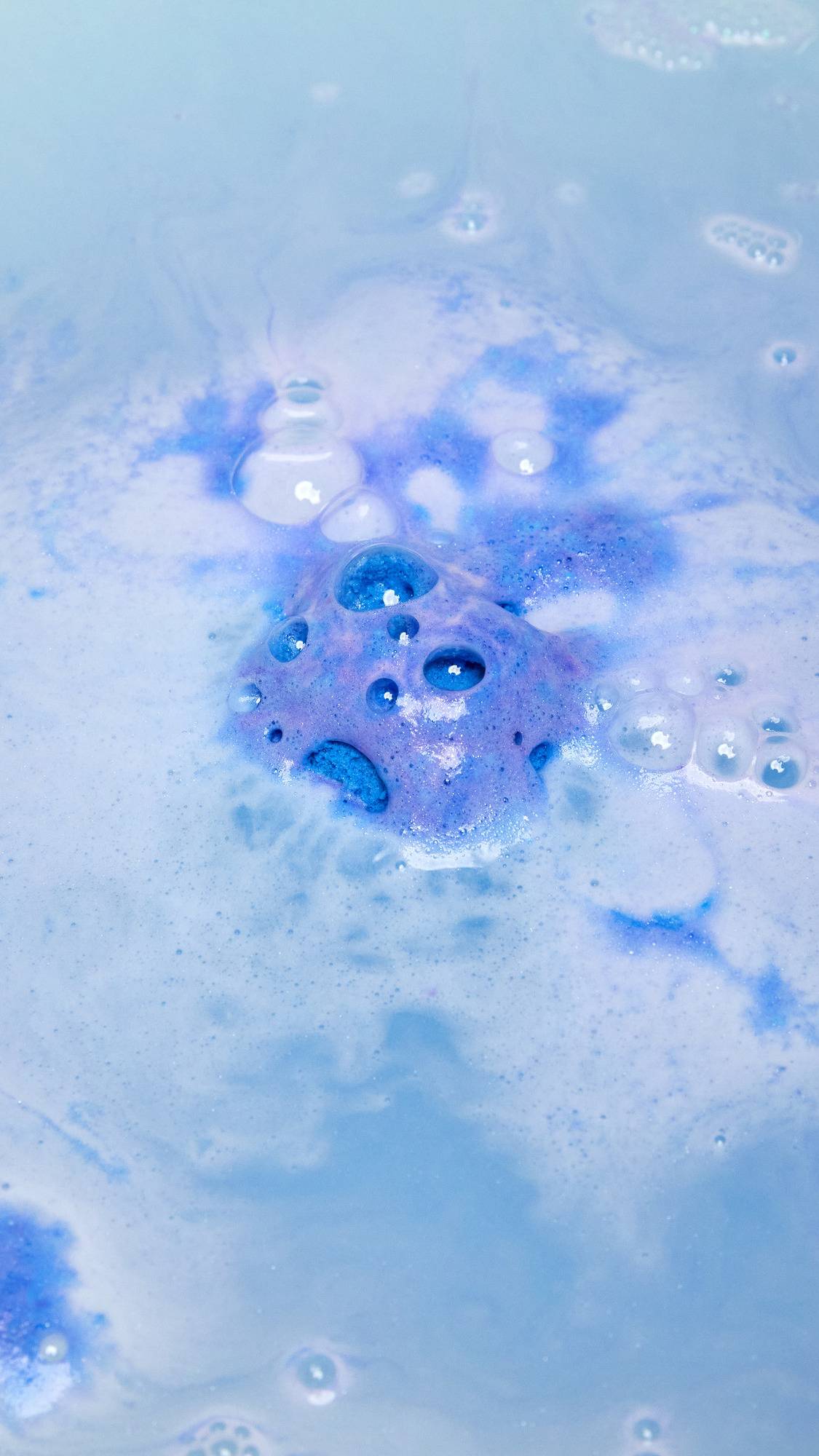 The Brother Moon bath bomb is slowly dissolving in the bath water as it starts to give off subtle purple and blue foam laced with silver sparkles.