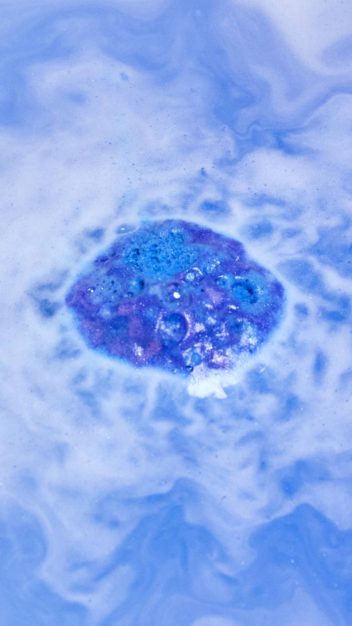 The Brother Moon bath bomb is slowly dissolving in the bath water as it starts to give off subtle purple and blue foam laced with silver sparkles.