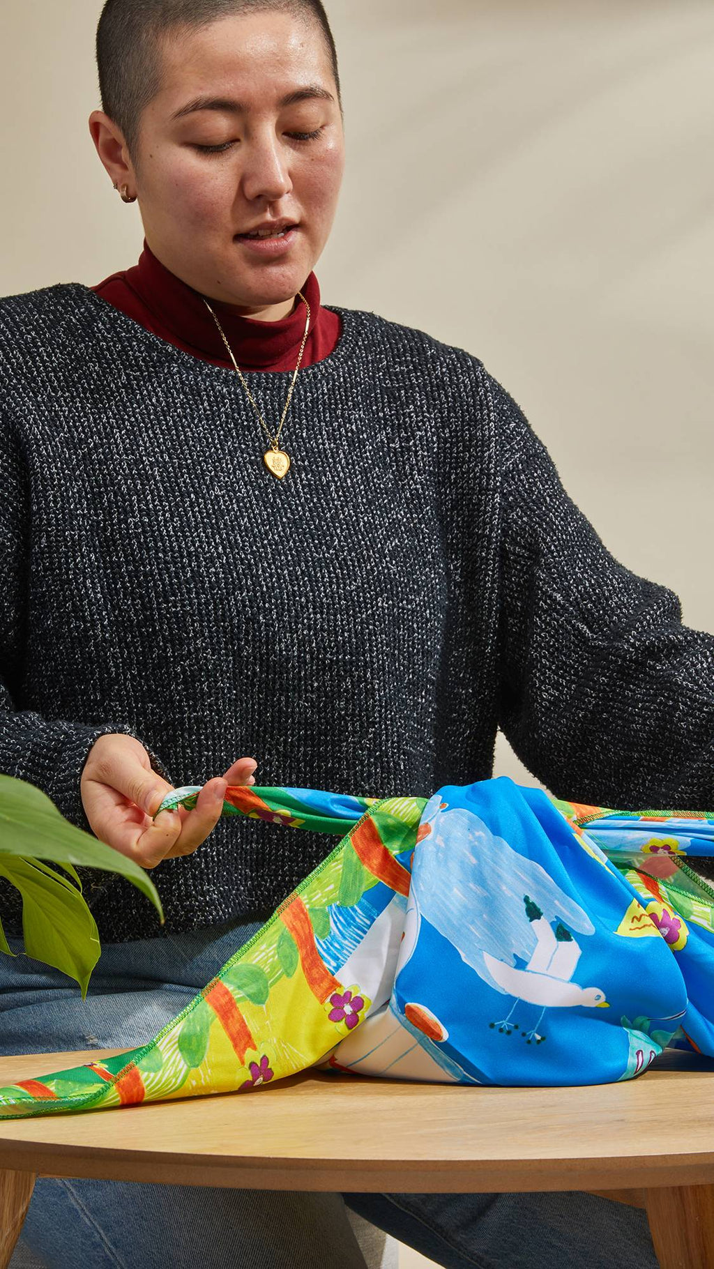The image shows the model as they sit at a table and neatly tie the By The Seaside knot wrap around a gift.