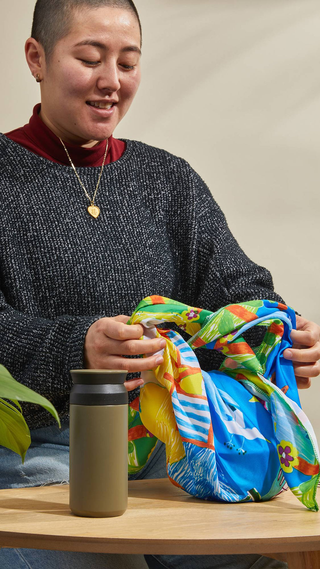 The image shows the model as they sit at a table and neatly tie the By The Seaside knot wrap around a gift.