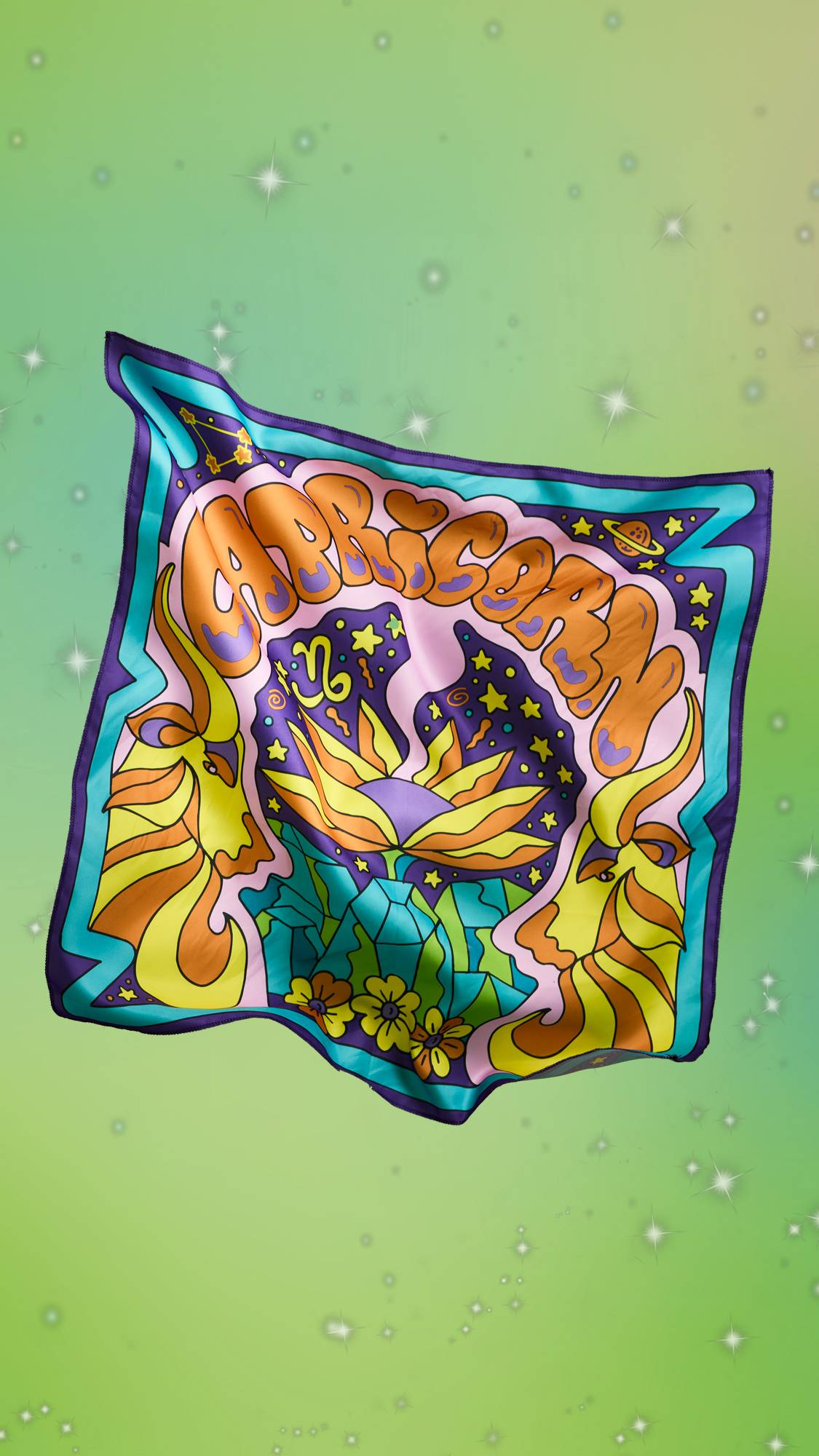 The image shows the colourful Capricorn fabric knot wrap suspended in front of a fresh, green, sparkling background. The knot wrap is facing forward showing the sheen of the fabric and vibrancy of colours.