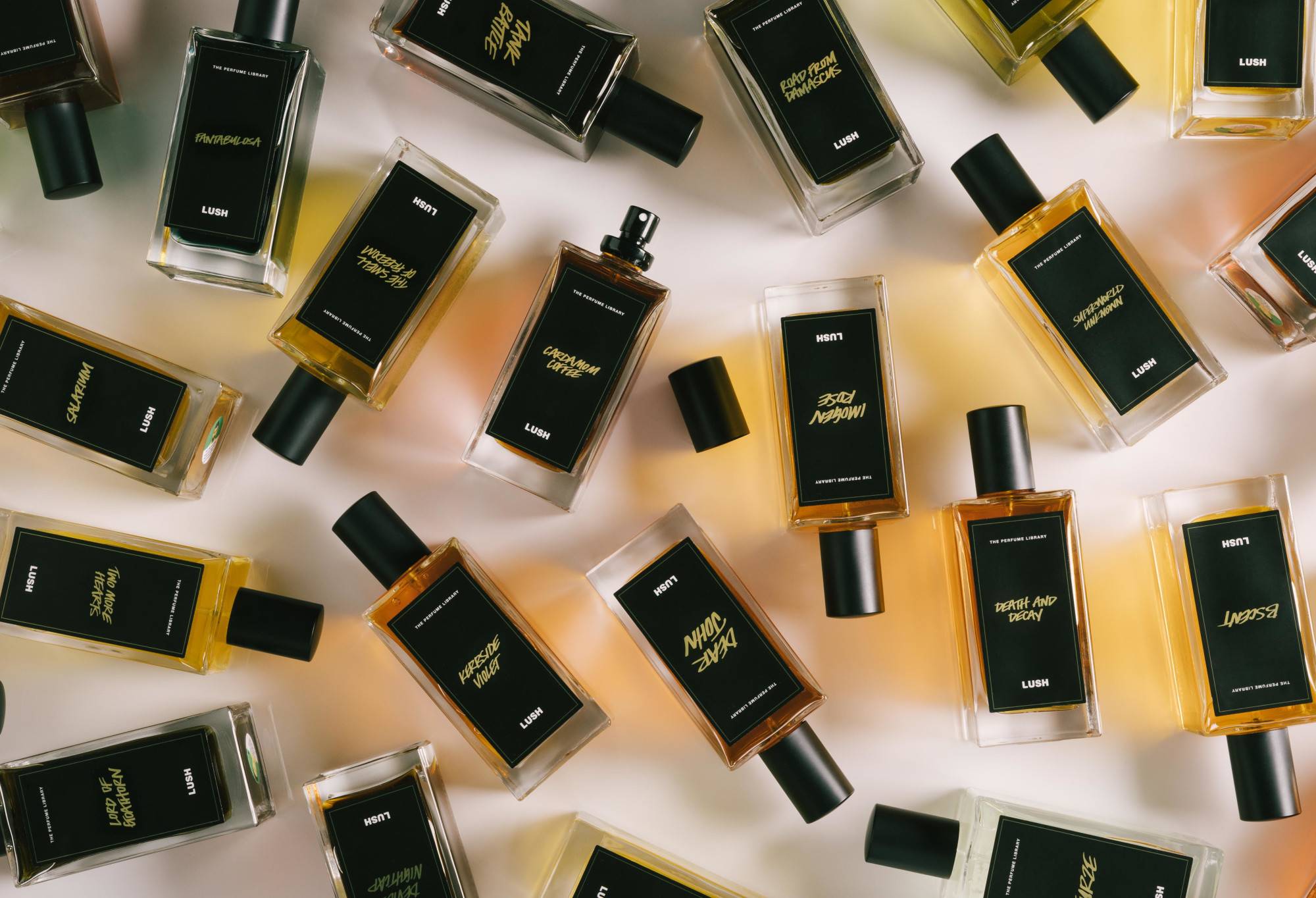 A number of black label perfume bottles are arranged randomly, with Cardamom Coffee in the centre, lid off, ready to spritz.