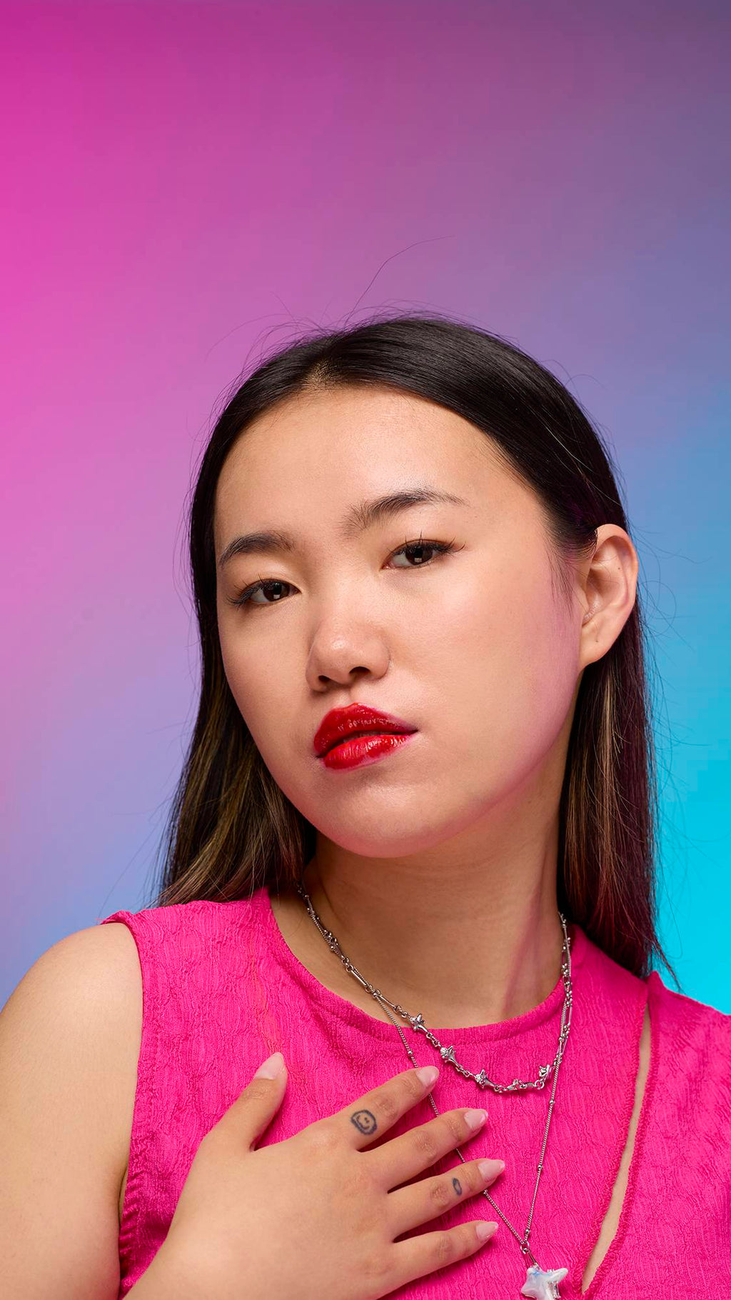 The model has long, straight dark hair and is on a pastel pink, blue and purple hue background. Their make-up has been done with the focal point being the juicy coating of cherry-red tint on their lips created by the Cherry lip jelly.