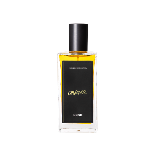 A glass perfume bottle filled with light amber liquid. A black label reads 'The Perfume Library' and 'Cocktail'.