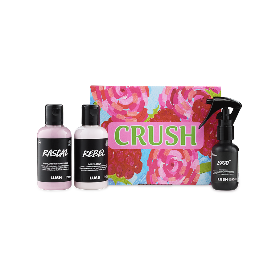 A LUSH Crush gift set featuring a brightly colored box with pink roses, next to three small black and white bottles: "Rascal" exfoliating shower gel, "Rebel" body lotion, and "Brat" body spray.