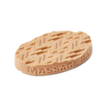 An oval, beige Lush solid massage bar featuring a raised zigzag texture on the top surface made of multiple "Z" letters and 'MASSAGE BAR' embossed along the side, set against a solid black background.