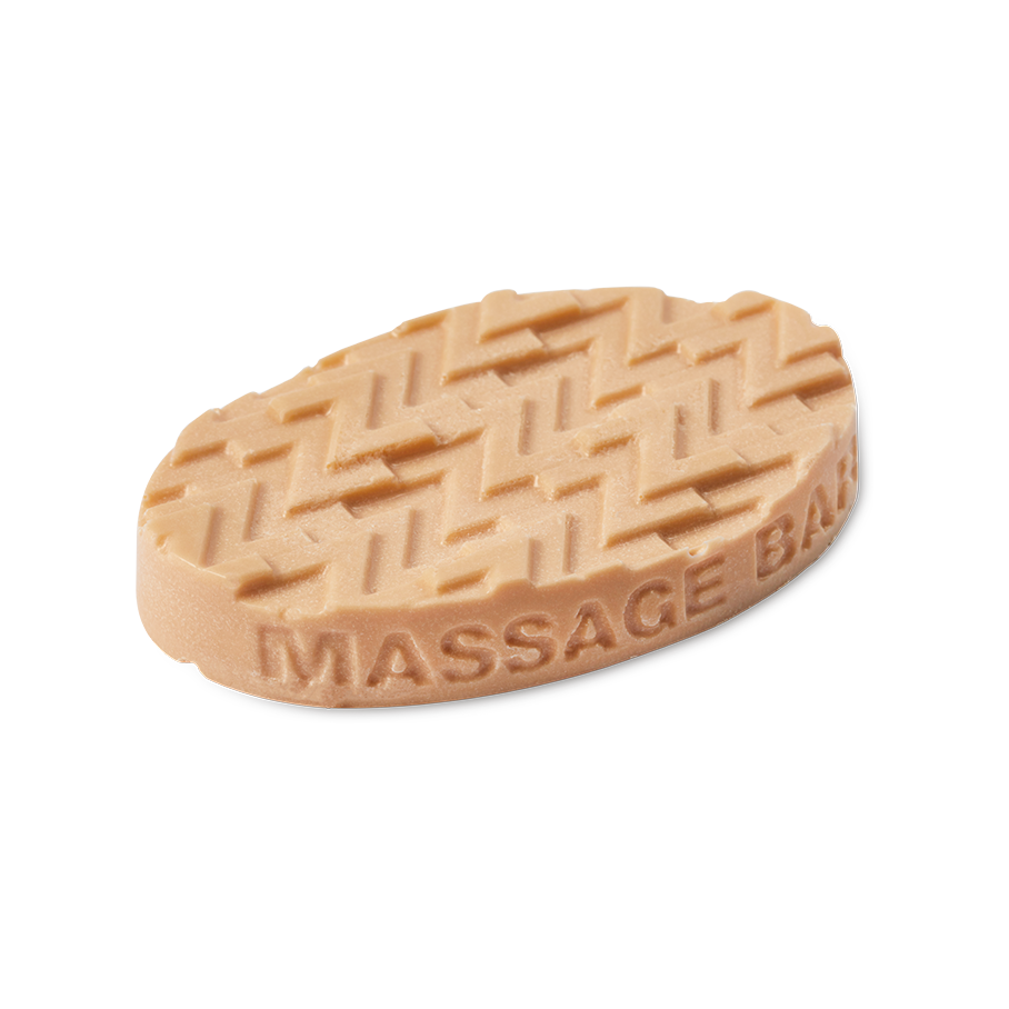 An oval, beige Lush solid massage bar featuring a raised zigzag texture on the top surface made of multiple "Z" letters and 'MASSAGE BAR' embossed along the side, set against a solid black background.