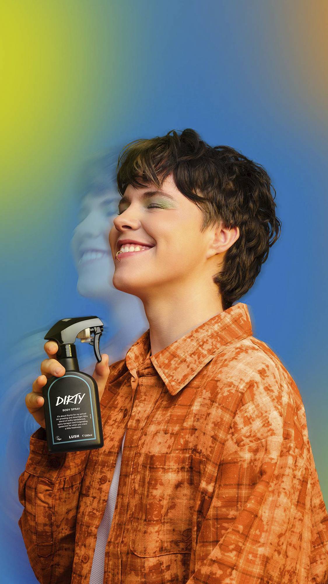 A smiling person with short wavy hair holds a black Lush 'Dirty' body spray. They wear an orange patterned shirt. A motion-blurred double exposure effect of their face floats behind them against a blue and yellow gradient background.