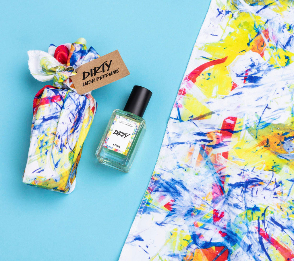 Dirty lies on a light blue background, alongside its two elements: a small bottle of Dirty perfume and a colourful knot wrap.