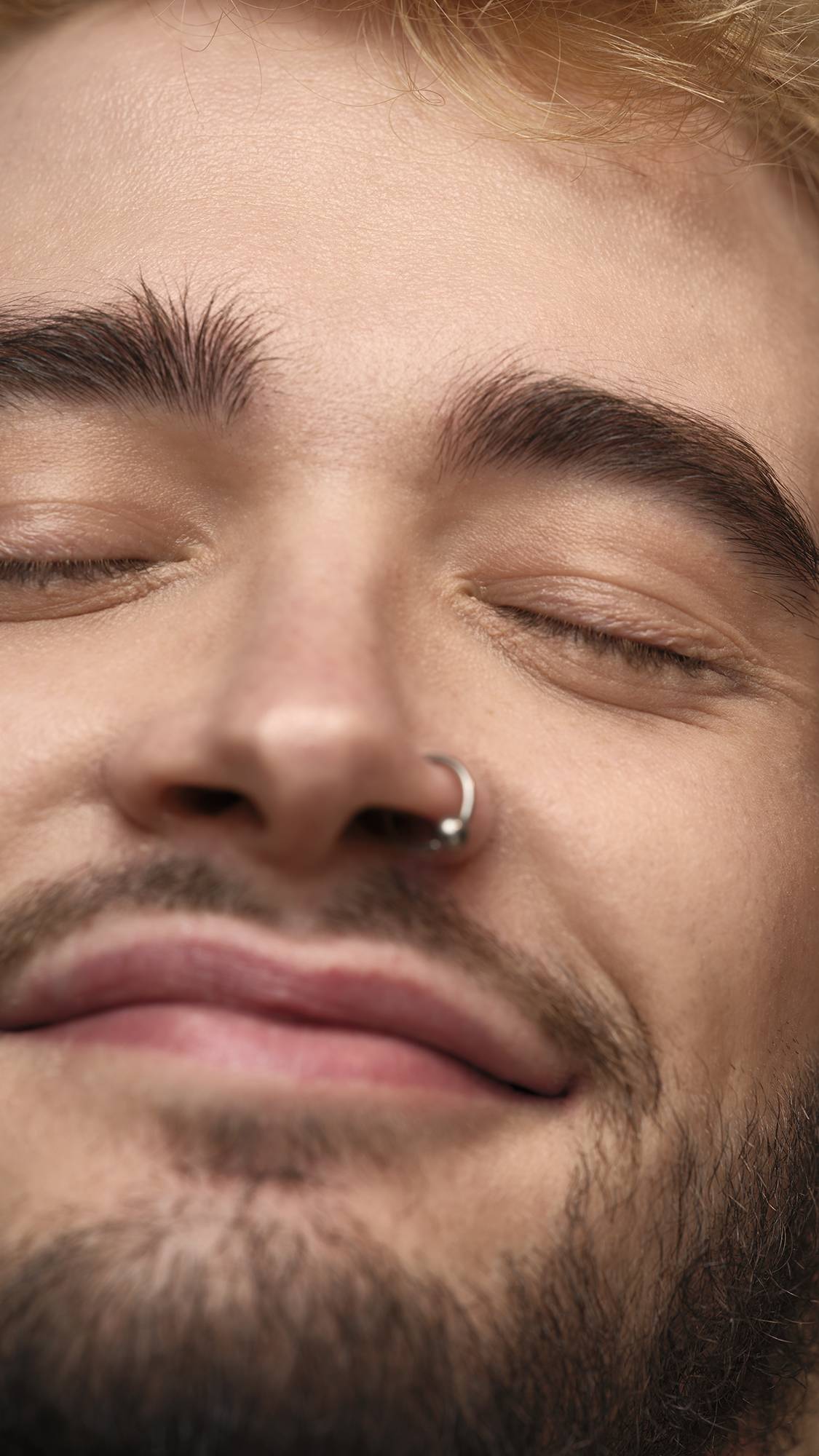 The model is on an earth-toned, warm background. They have their eyes closed as they are smiling at the camera with glowing, freshly moisturised skin and bright under-eyes.